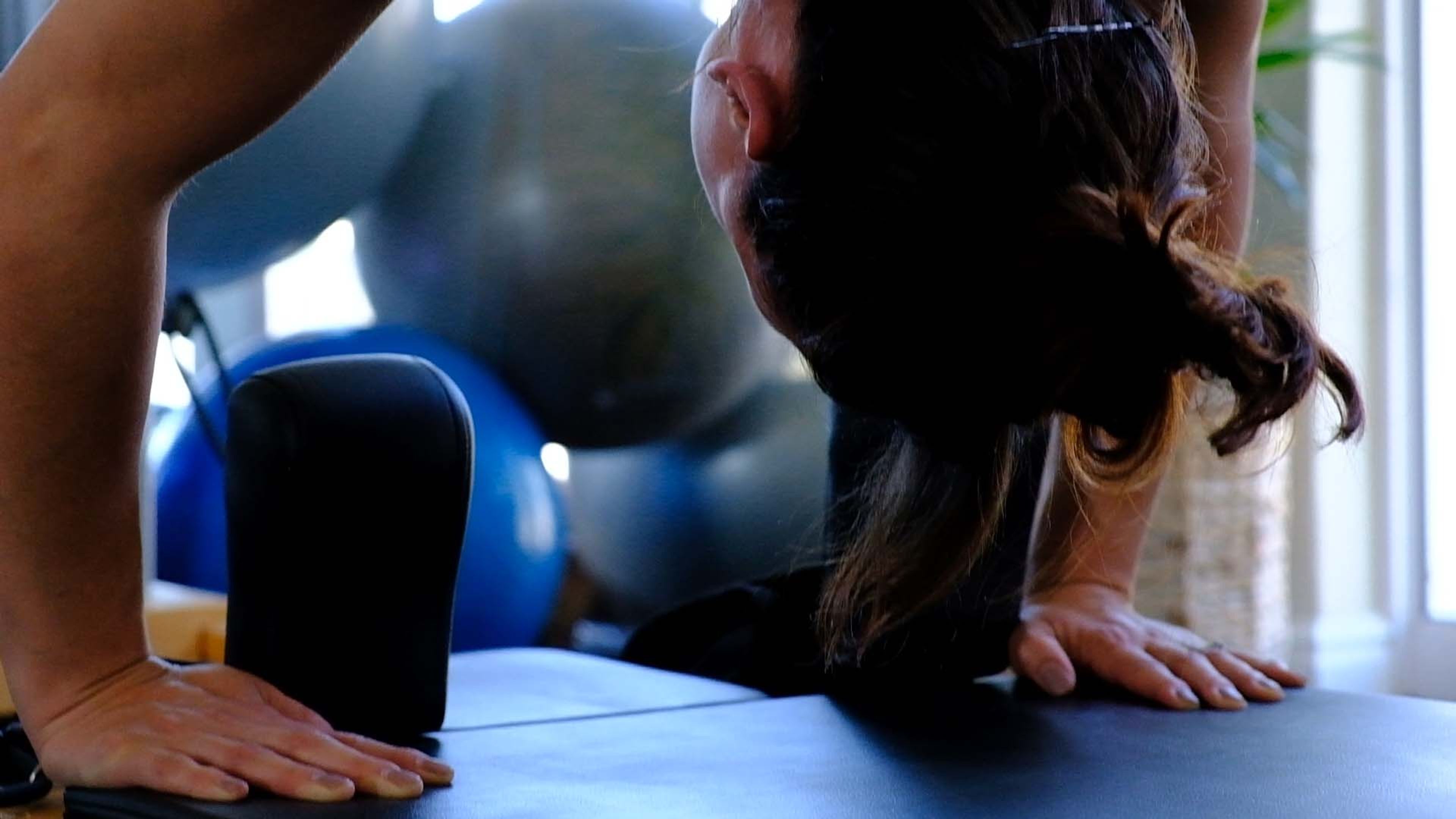 Woman in an upside-down stretch over a Pilates box with stability balls behind her