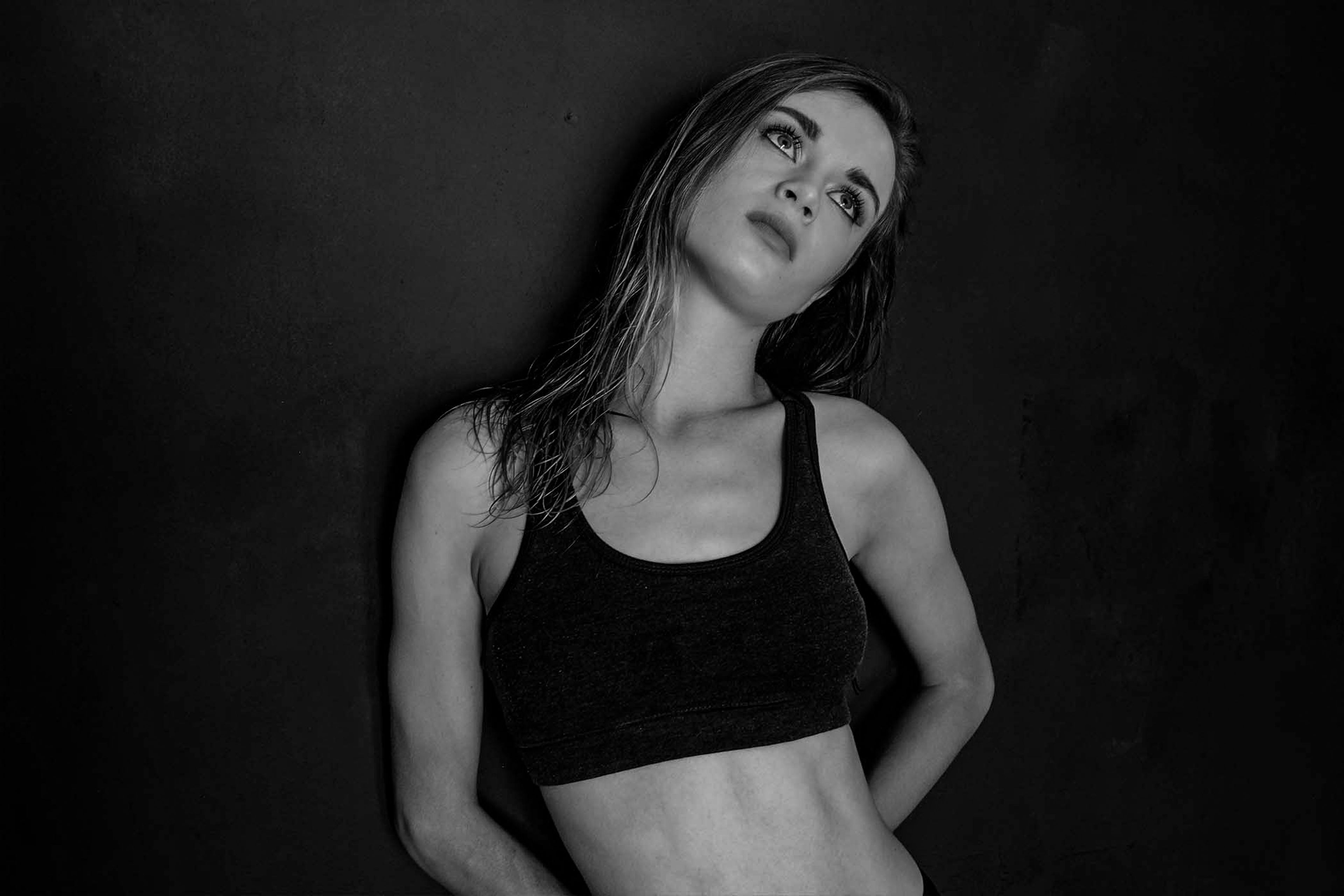 Black and white portrait, subject in a fitted sports bra looking upward against a dark backdrop