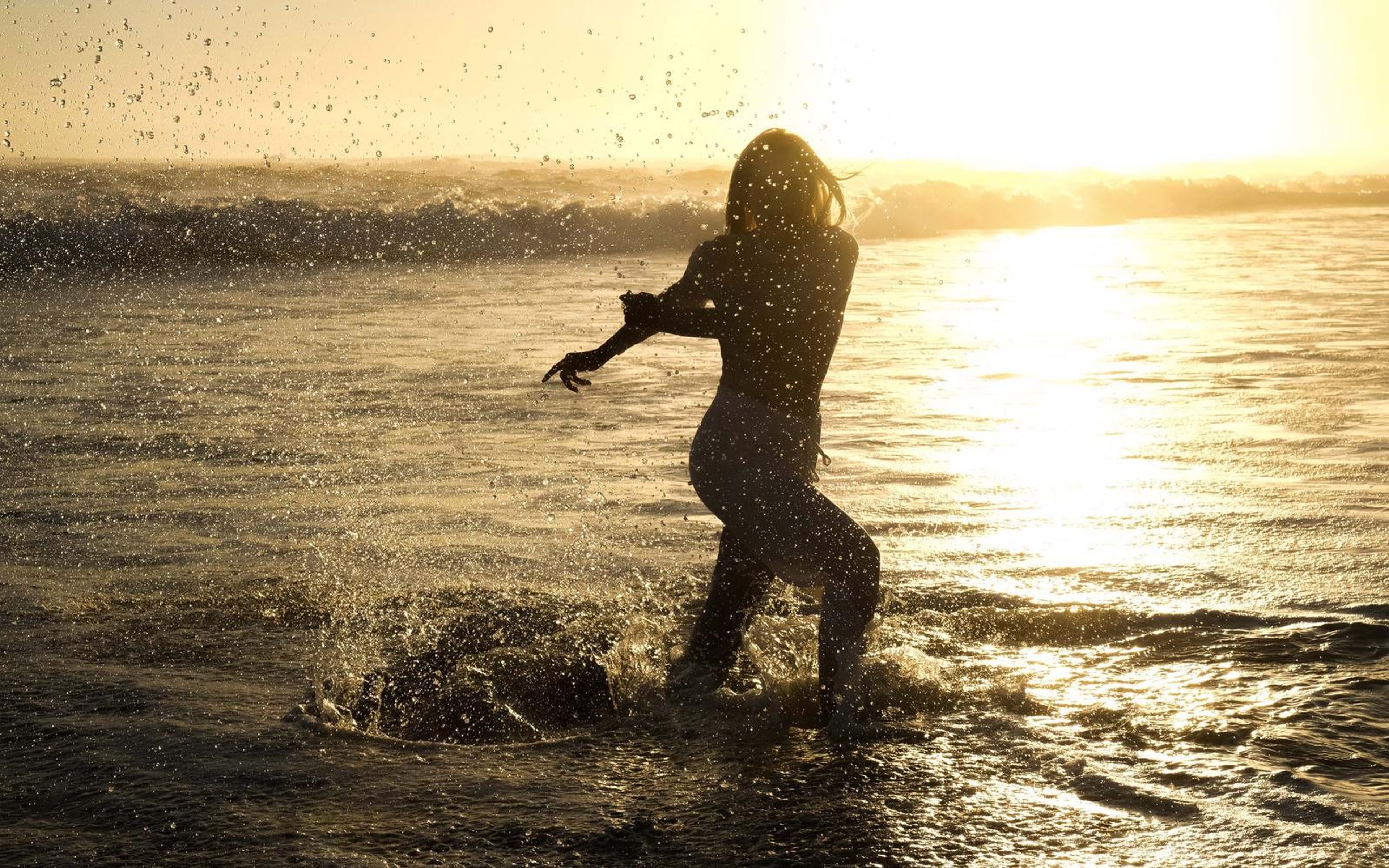 Woman splashing in the surf with water droplets flying against the sunset glow