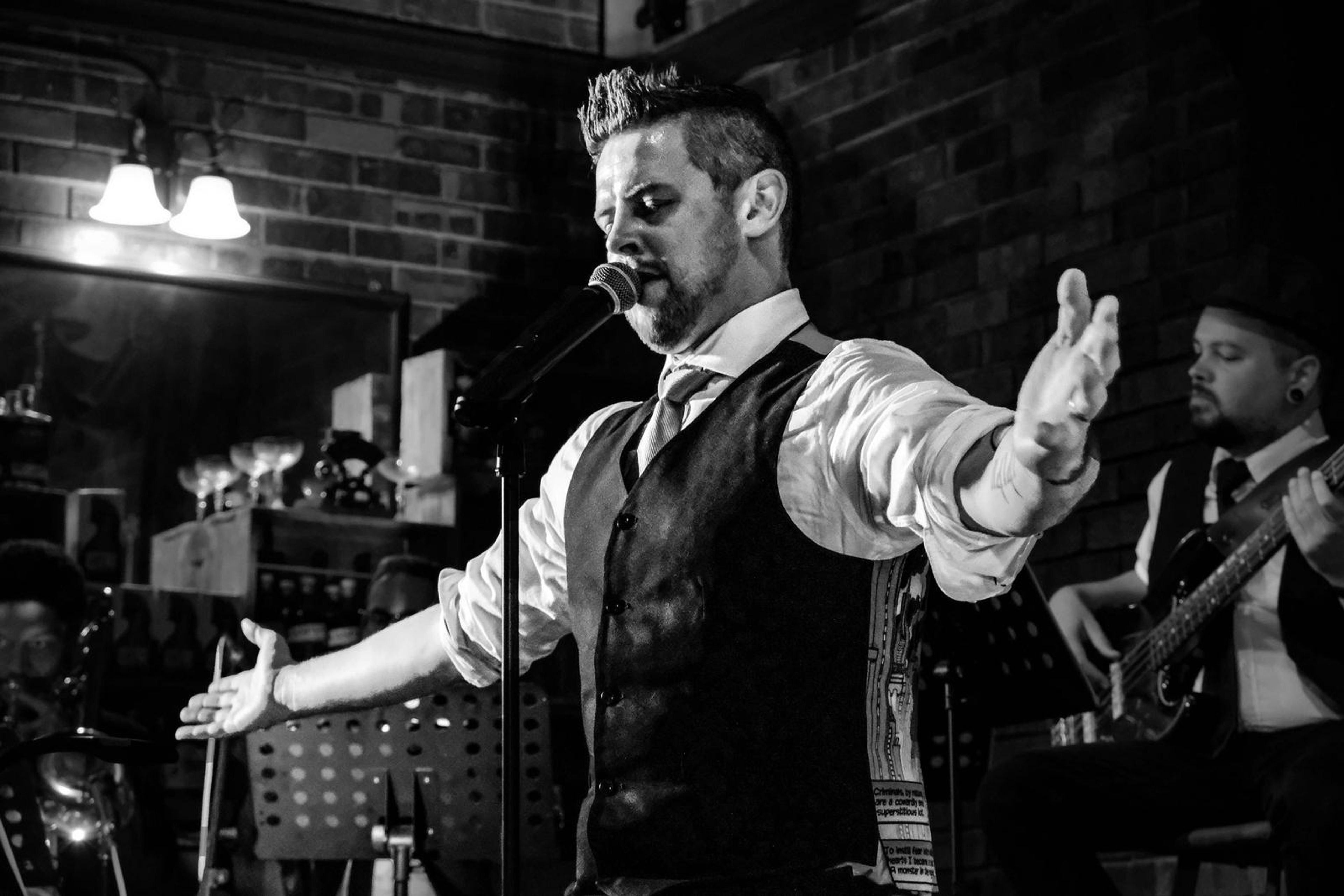 Black and white version of the lead singer with his arms spread wide while the band plays behind him