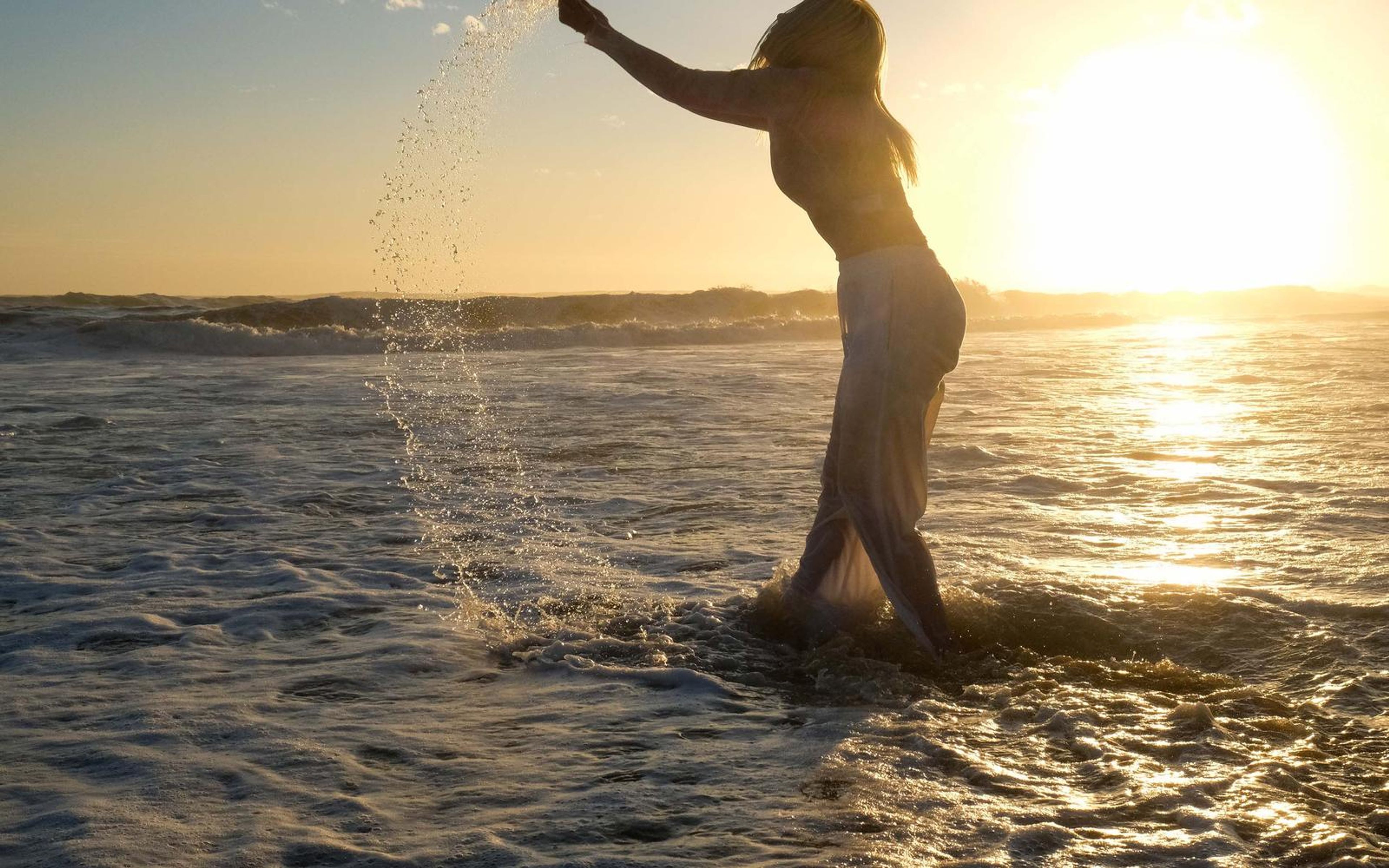 Woman in silhouette throwing a splash of water in the surf at sunset