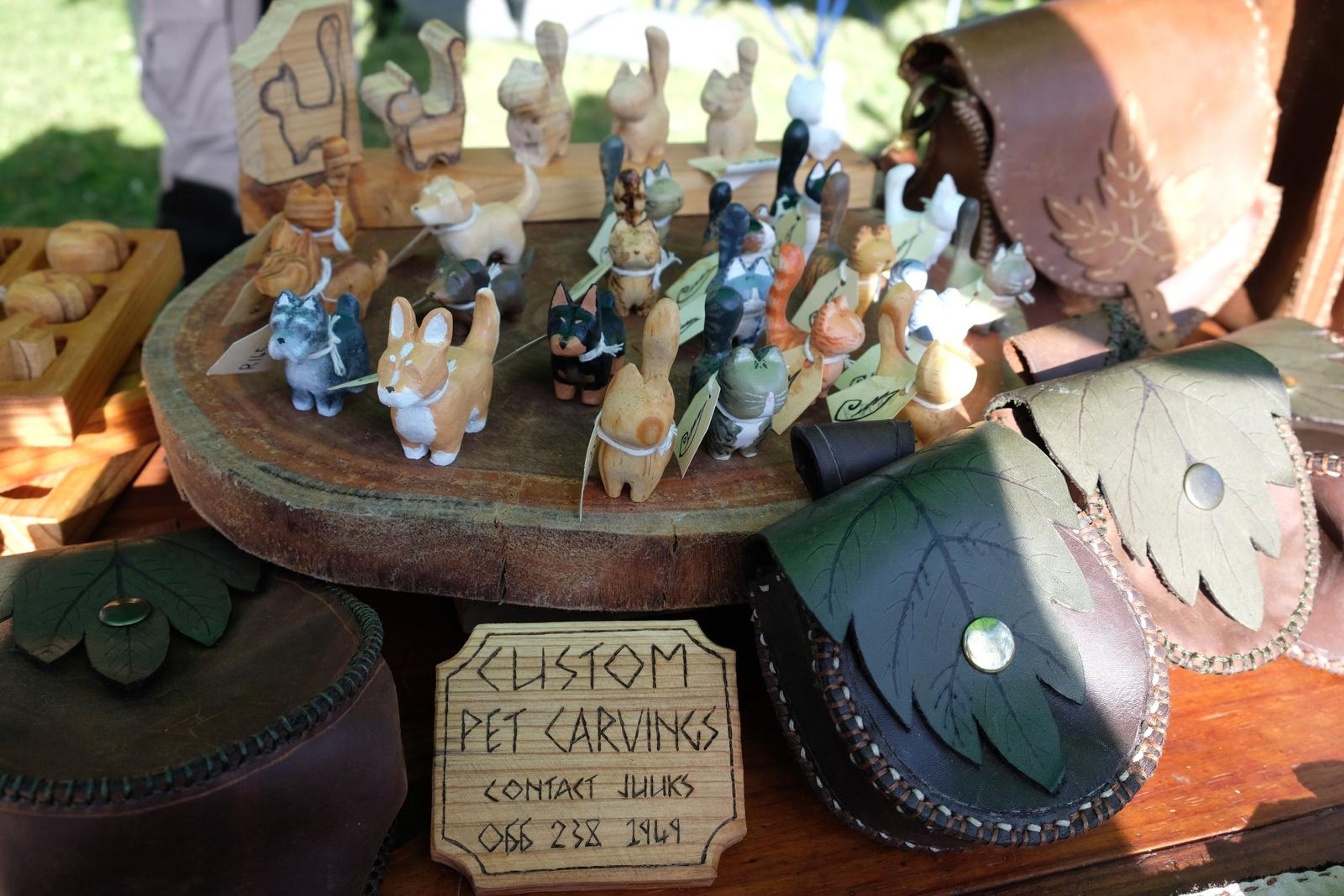 Custom Pet Carvings display with carved figures and black leaf-shaped leather pouches