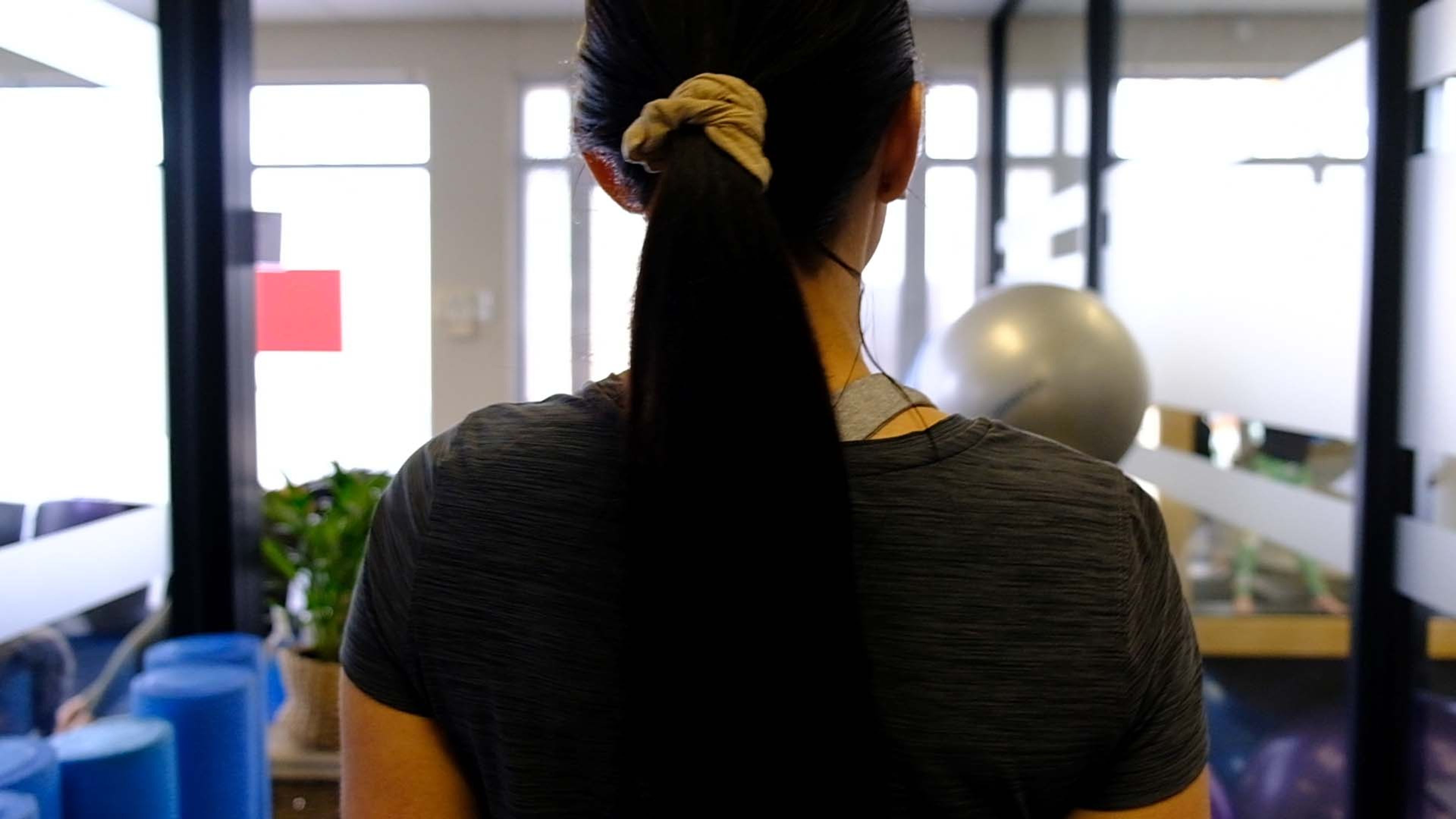 Staff member seen from behind in the studio with stability balls and foam rollers beside her