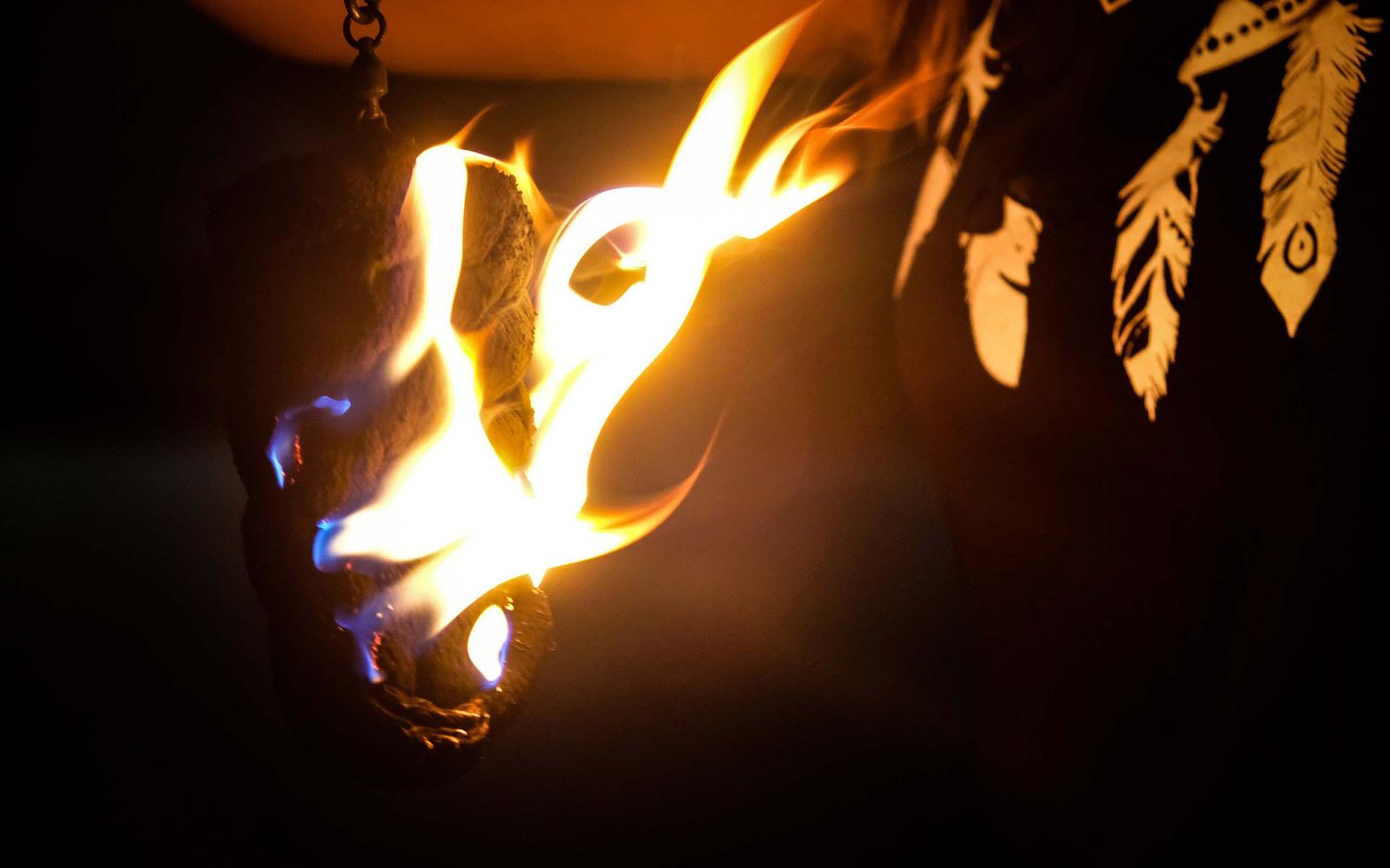 Close-up of a large flame on a hanging prop beside a dark top with a feather print