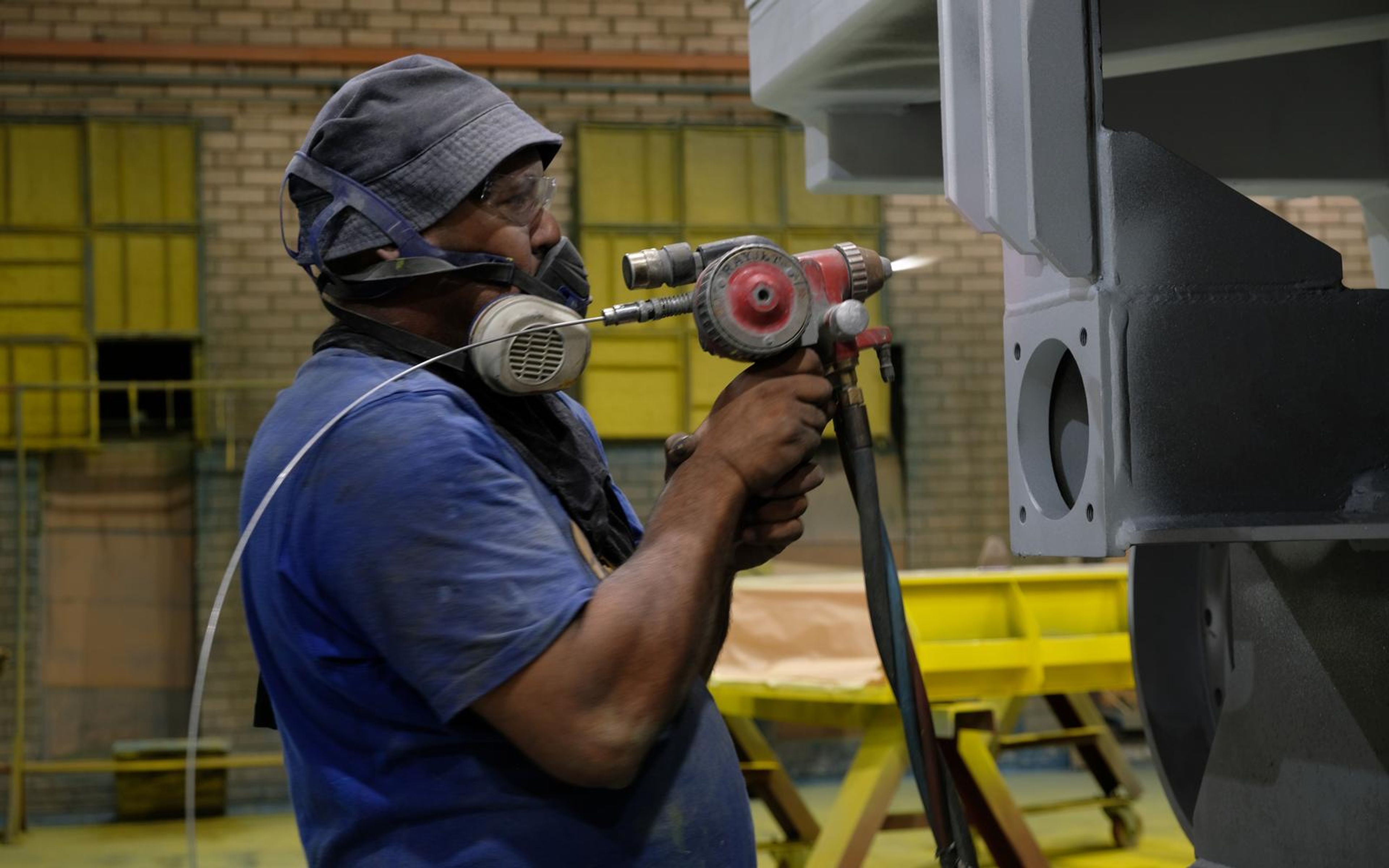 Painter in a respirator holding a spray gun beside a steel part