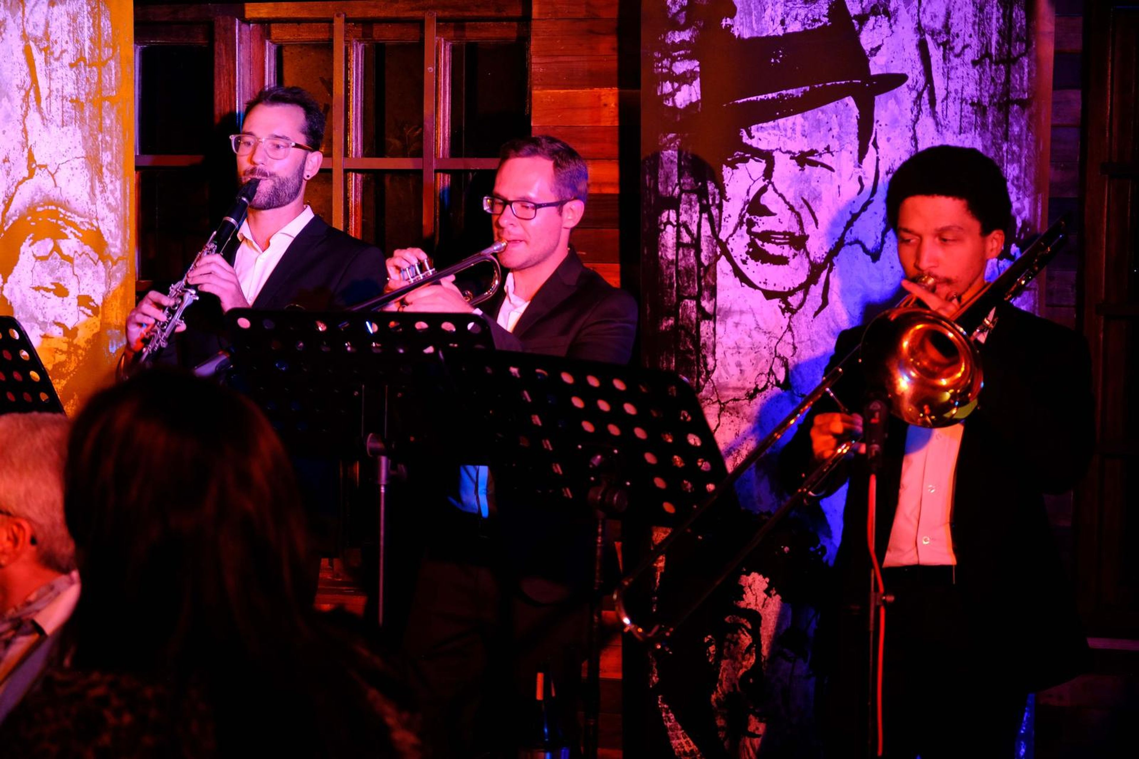 Clarinet, trumpet and trombone players in front of a mural