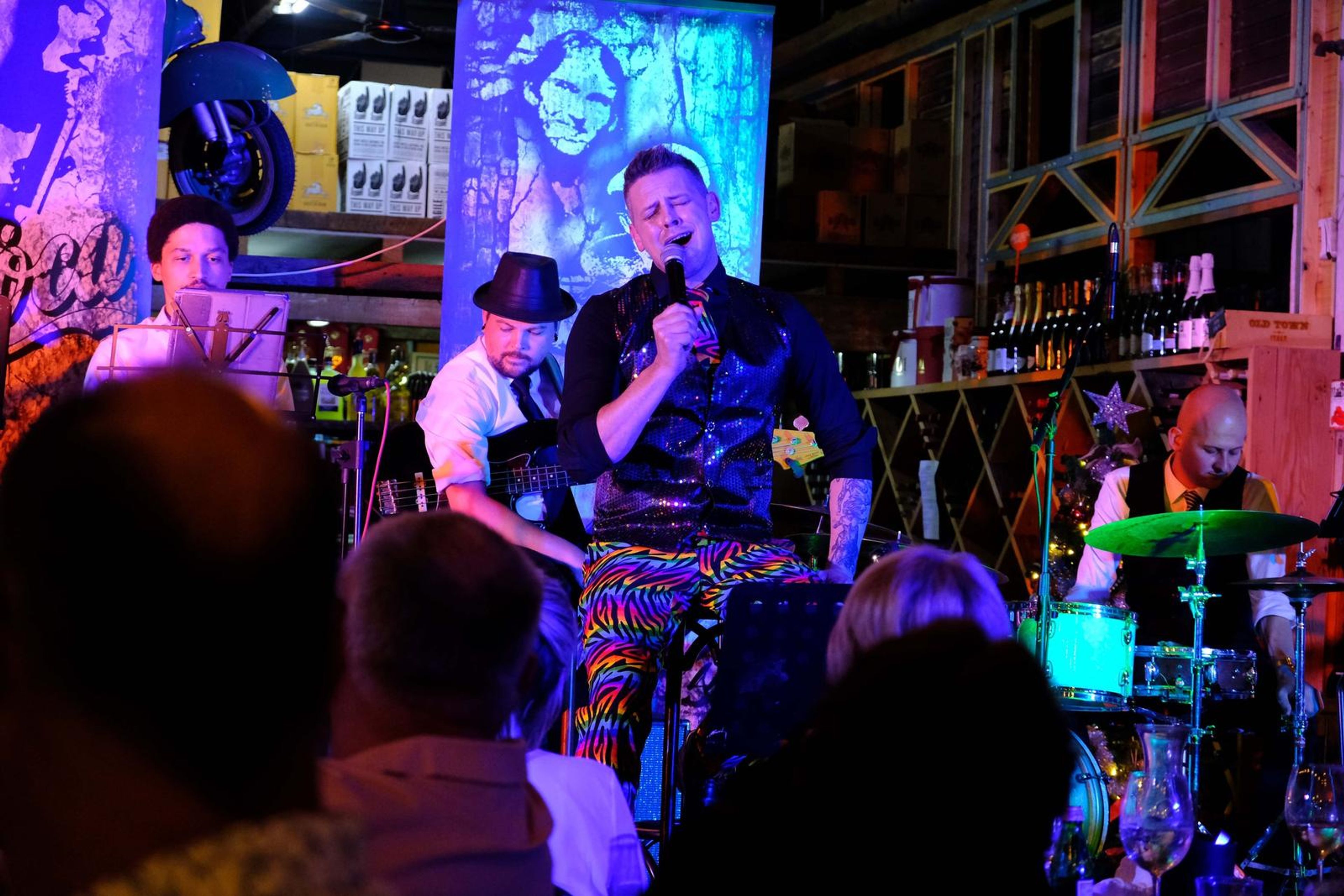 Singer in a waistcoat singing in front of a mural, with the crowd in the foreground