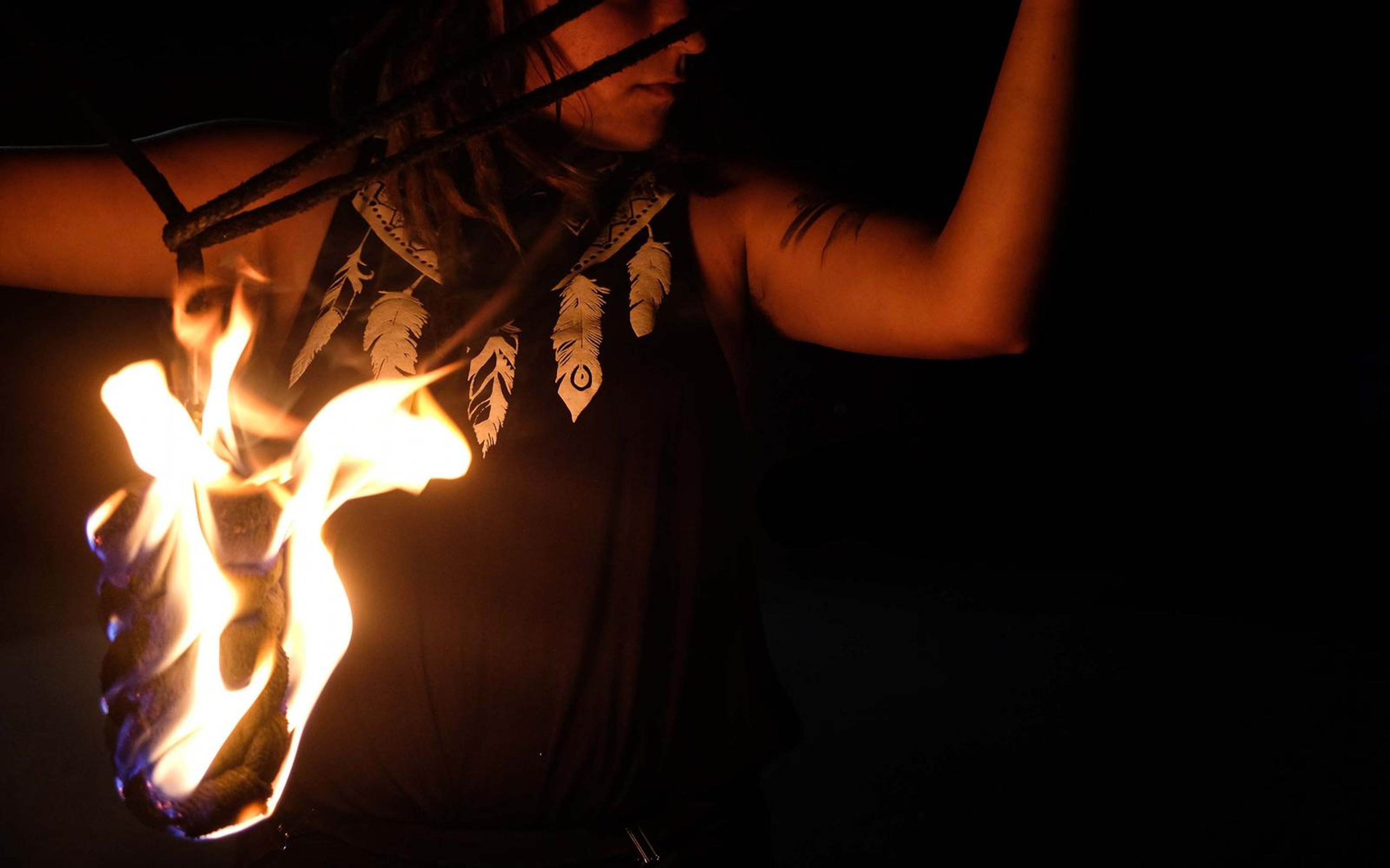 Large flame rising from a prop in front of a feather-print top, arms raised, face cropped