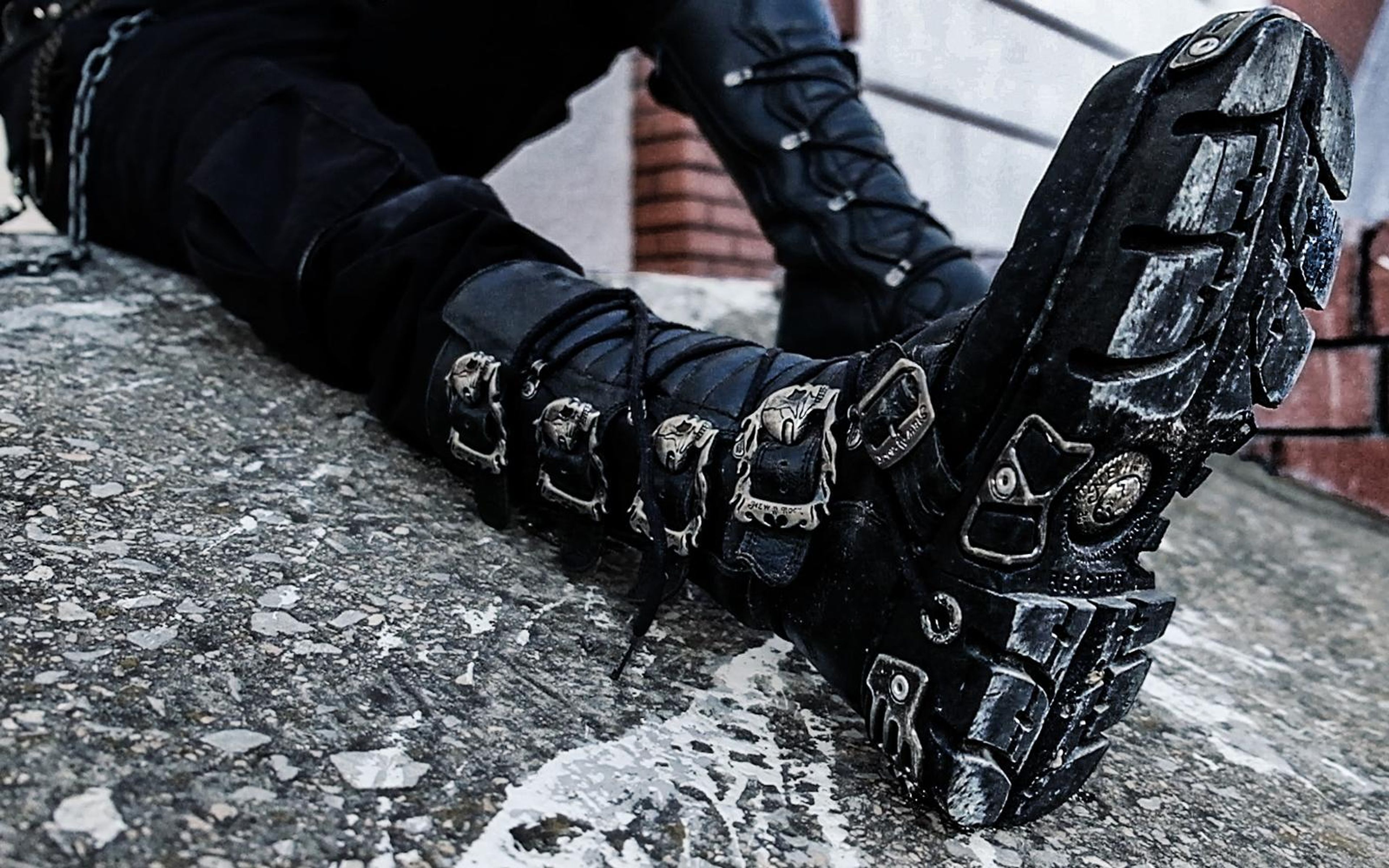 Laced, buckled boot with its sole facing camera, performer lying on a rough concrete slab