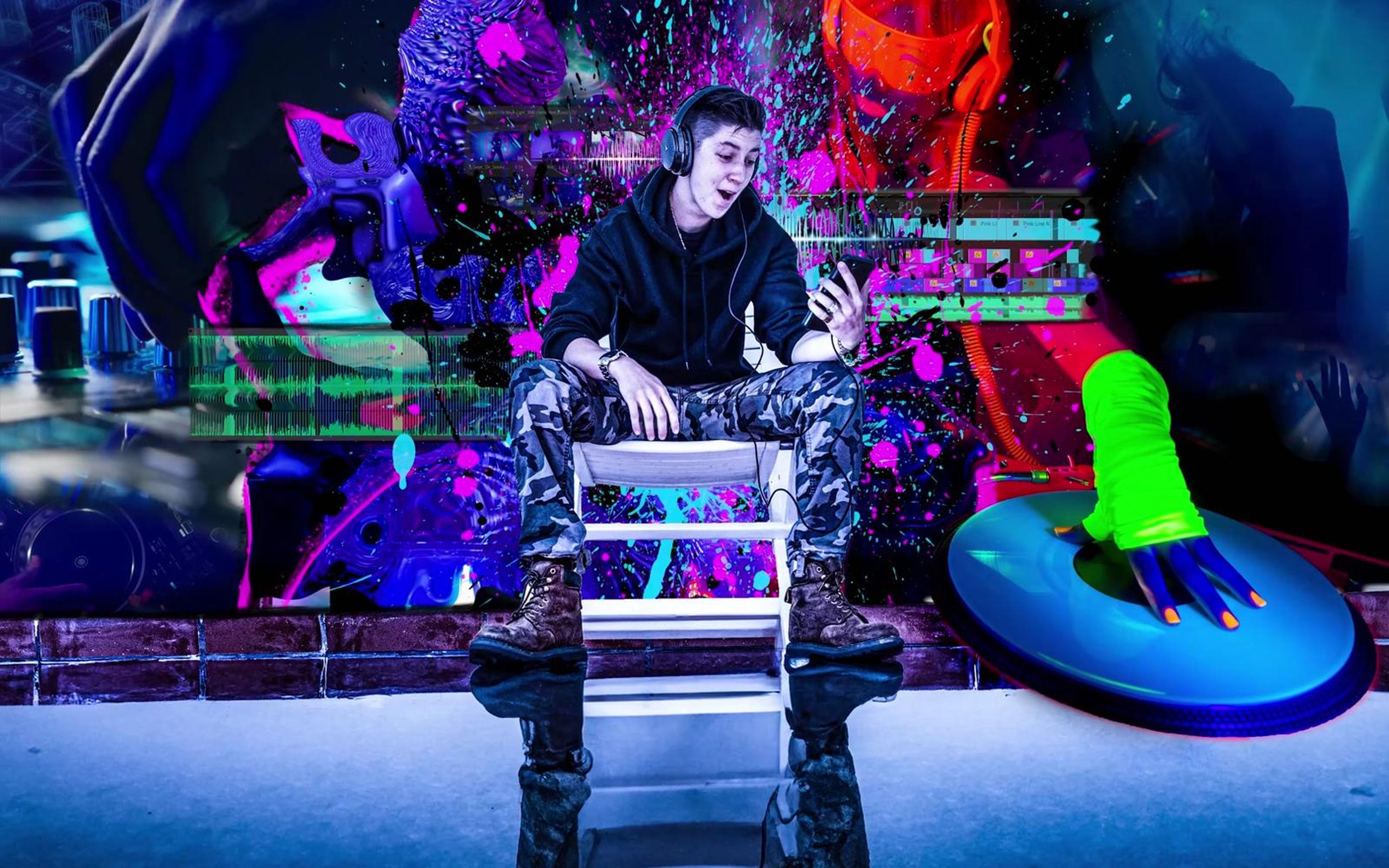 Seated man in camouflage trousers surrounded by magenta and cyan paint splatter, blue reflective floor below