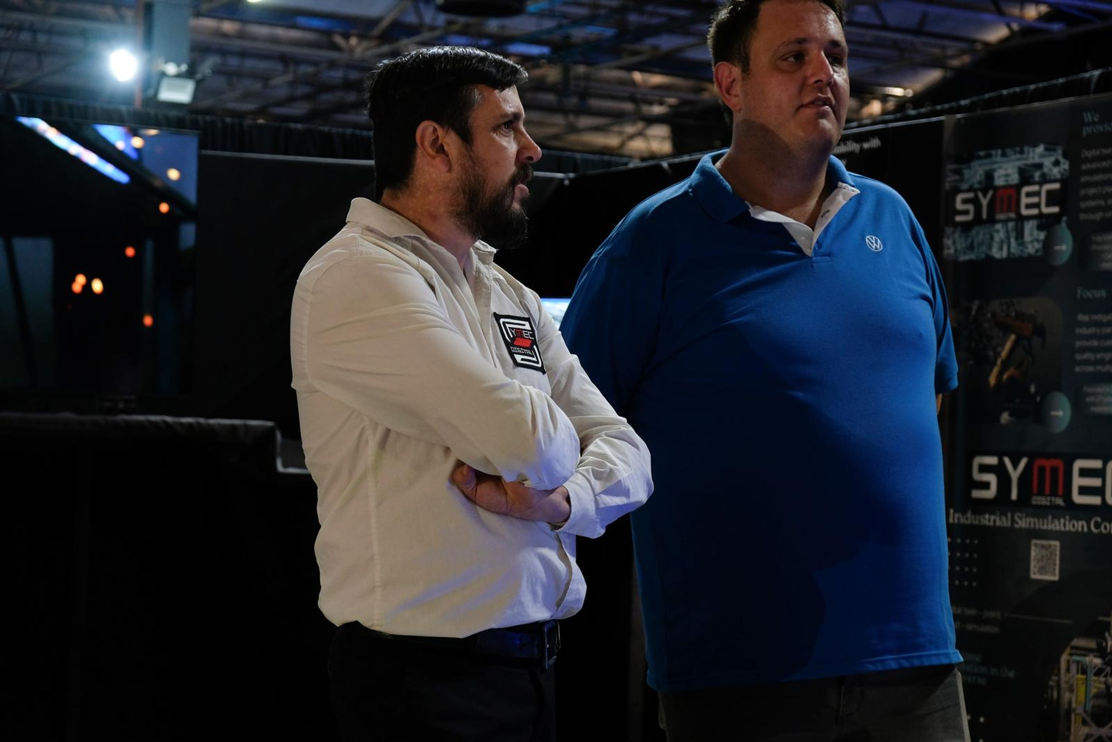 Two men in conversation in front of the Symec display wall