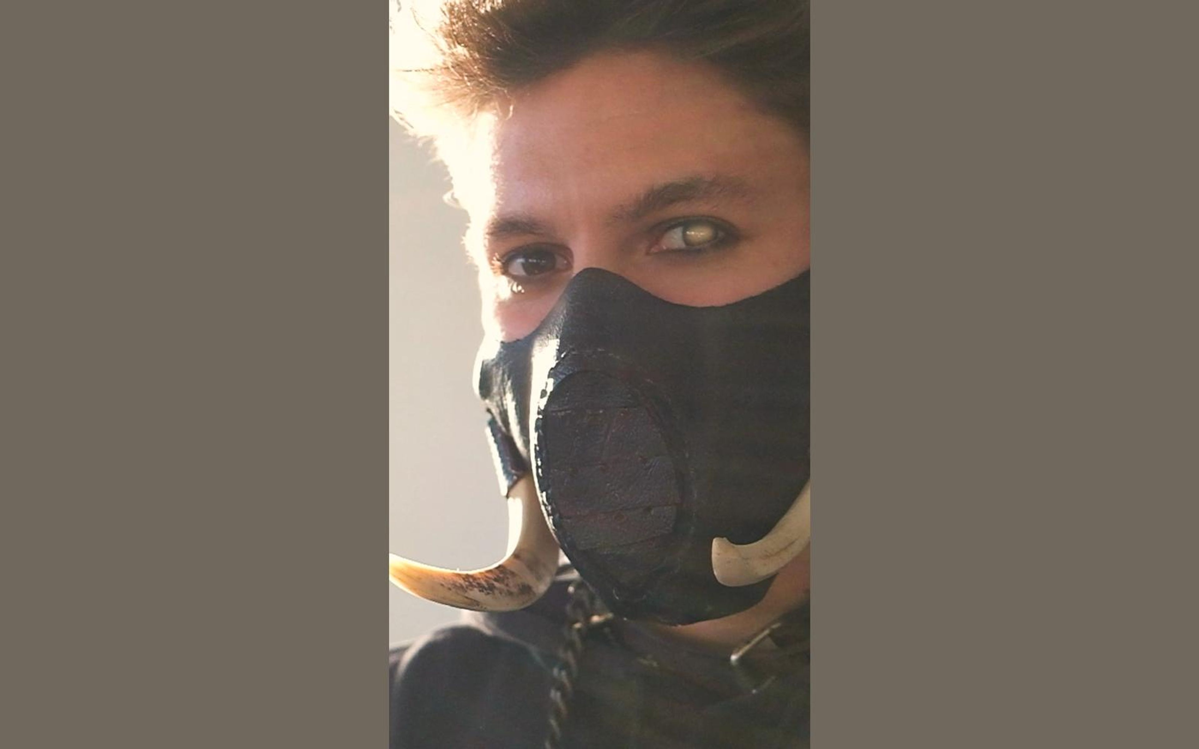 Intense close view of the warrior's eyes above the tusked mask in warm, hazy light