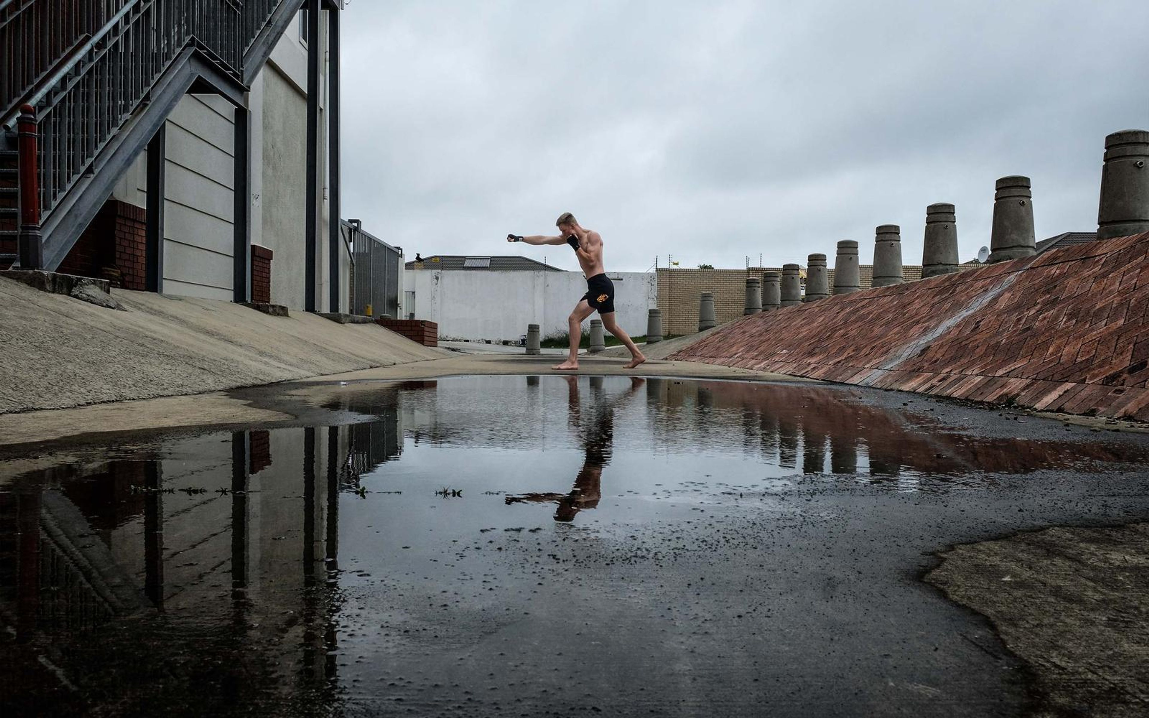 Fighter throwing a punch beside a large puddle on a concrete ramp with industrial buildings behind