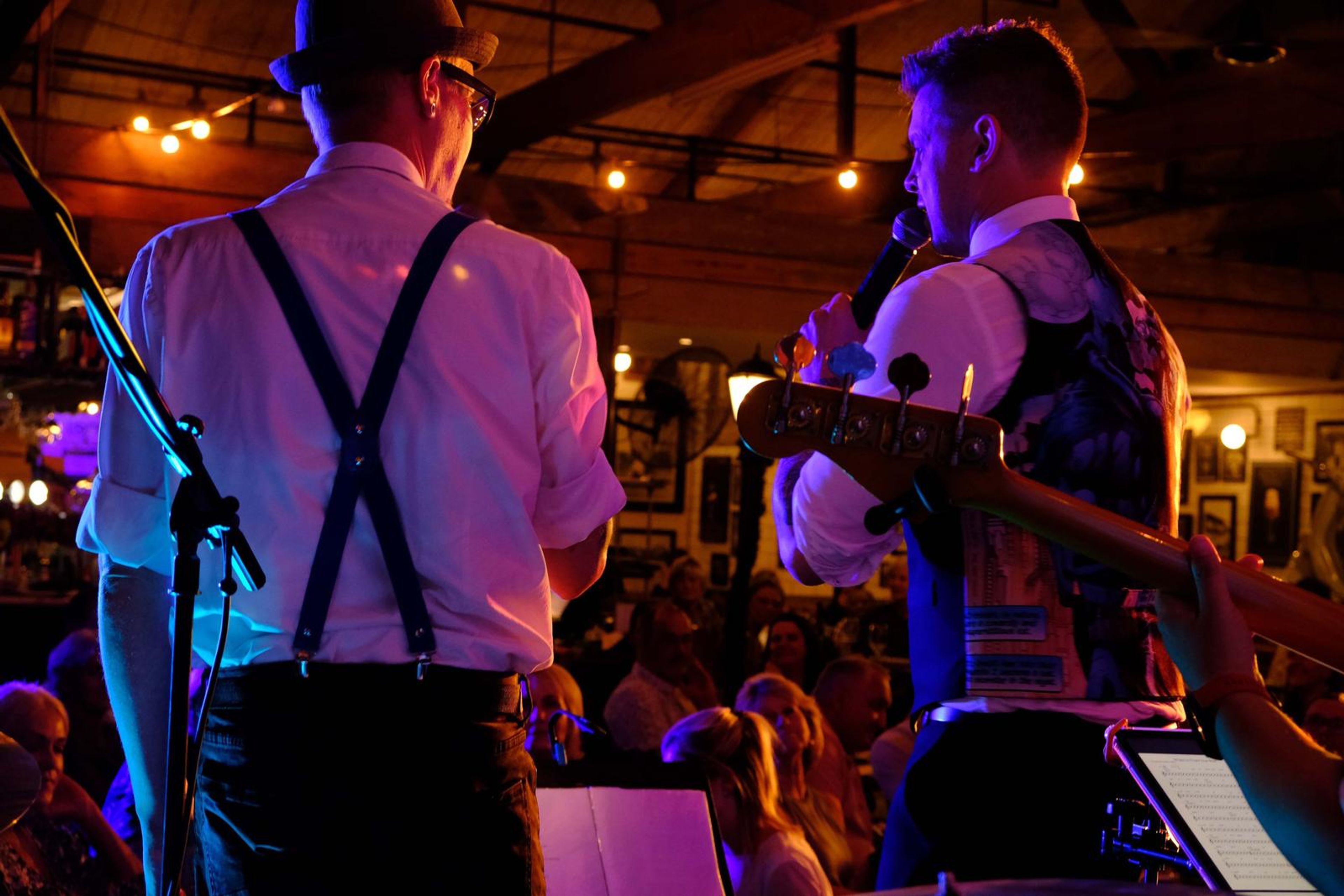Two band members in hats and suspenders seen from behind