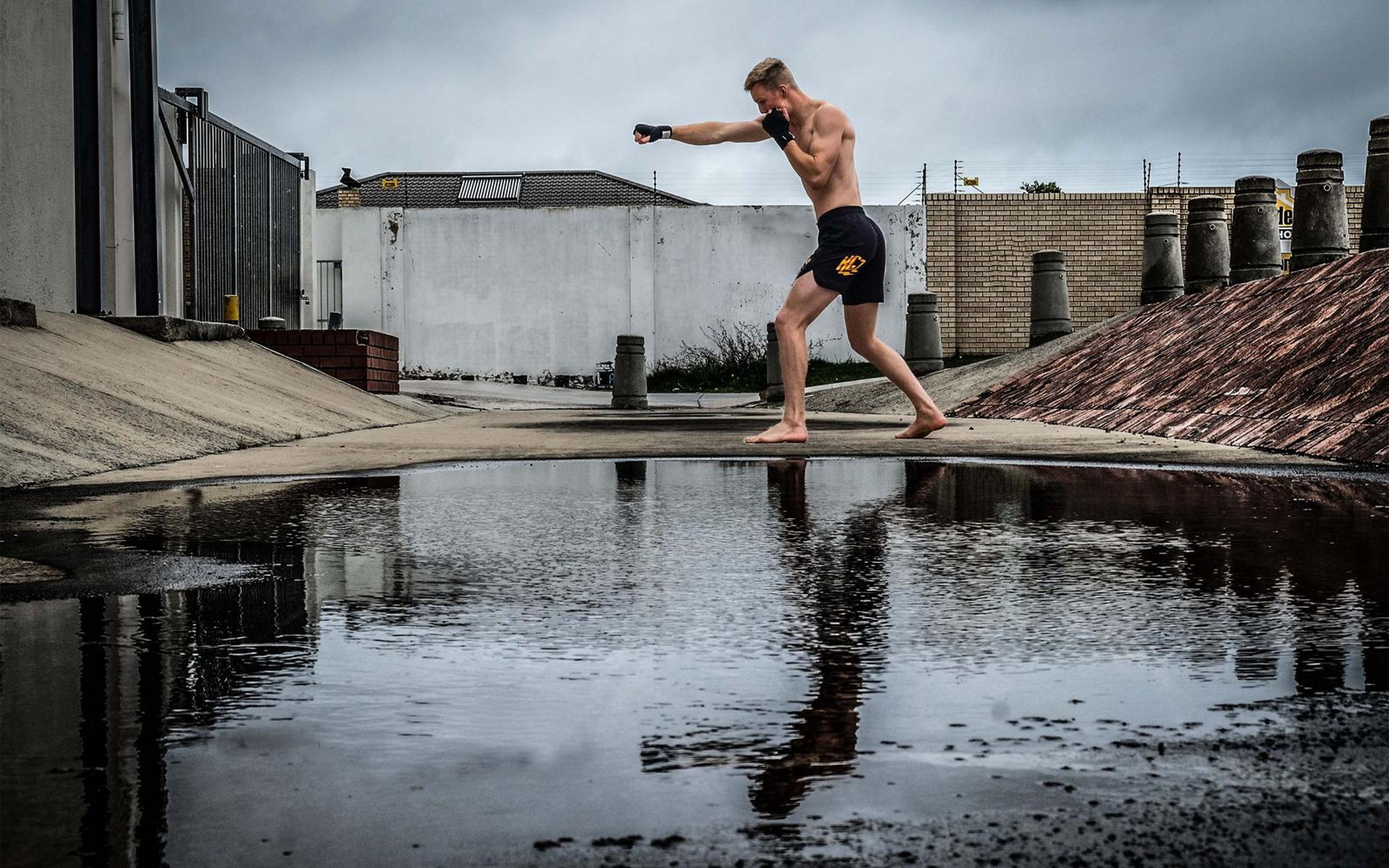 Man throwing a jab in a wide stance by a puddle, wet ground and cloudy sky