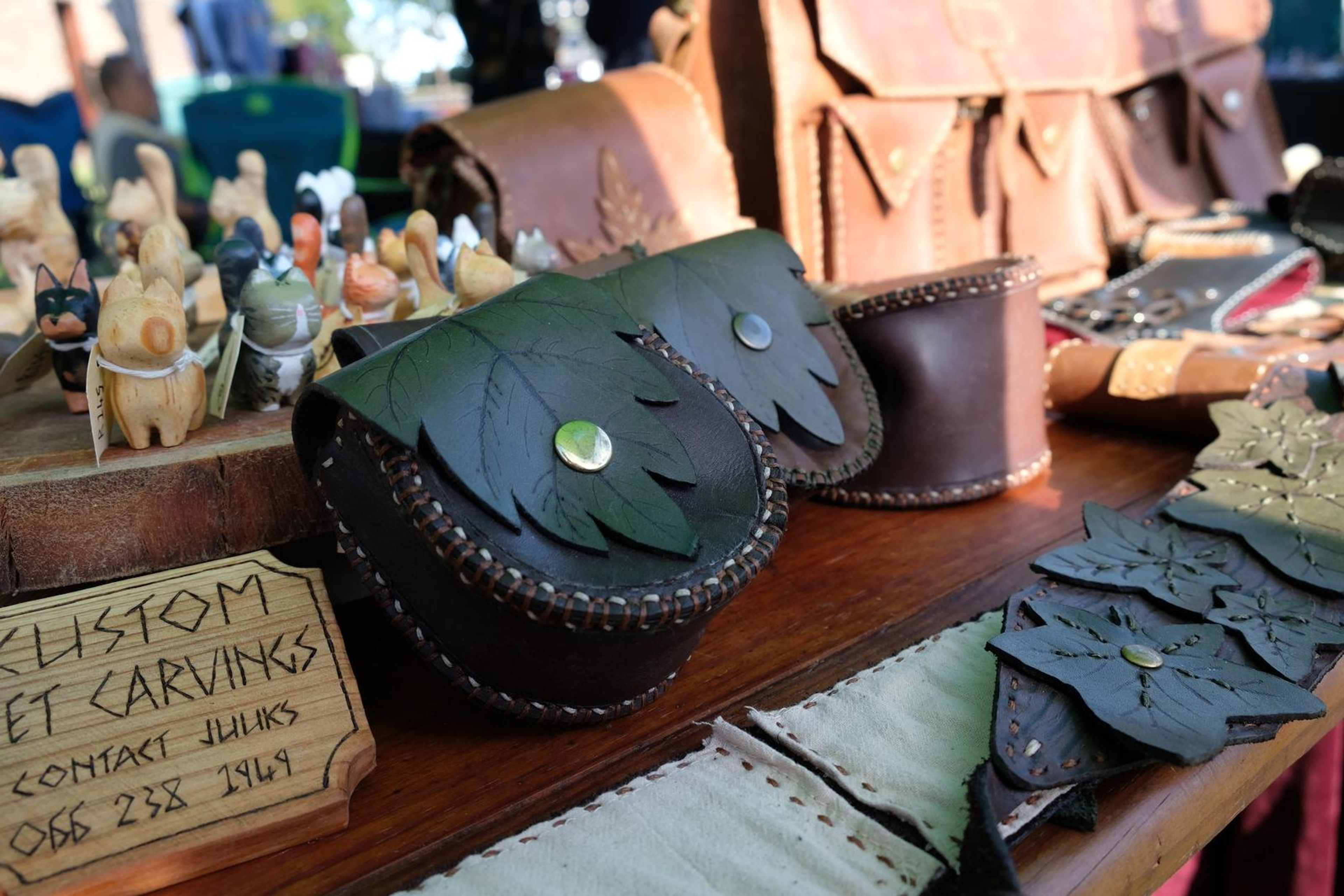 Black leaf-shaped leather pouches beside carved figures and a Custom Pet Carvings sign