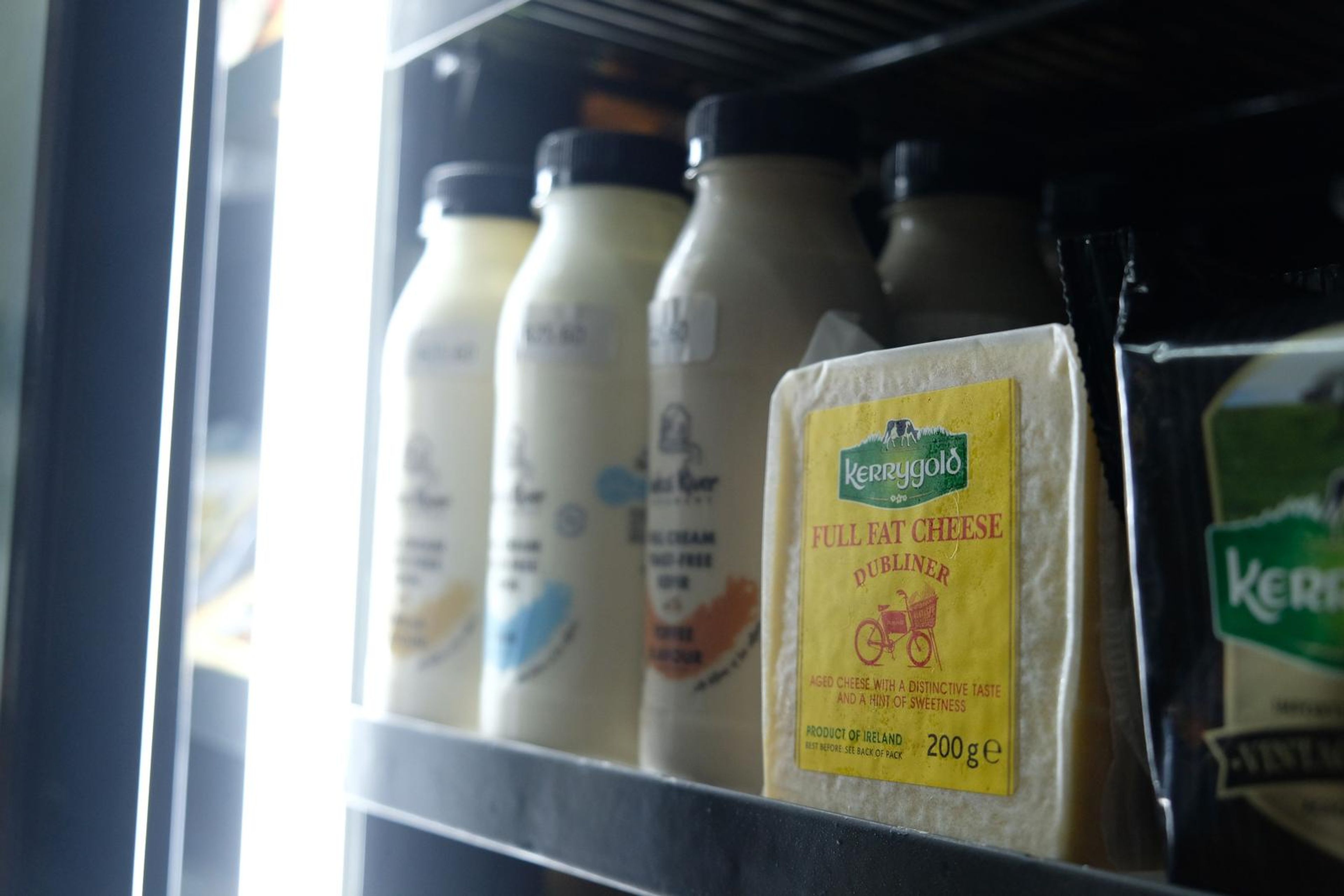 Wedge of yellow cheese beside bottles of milk in the fridge