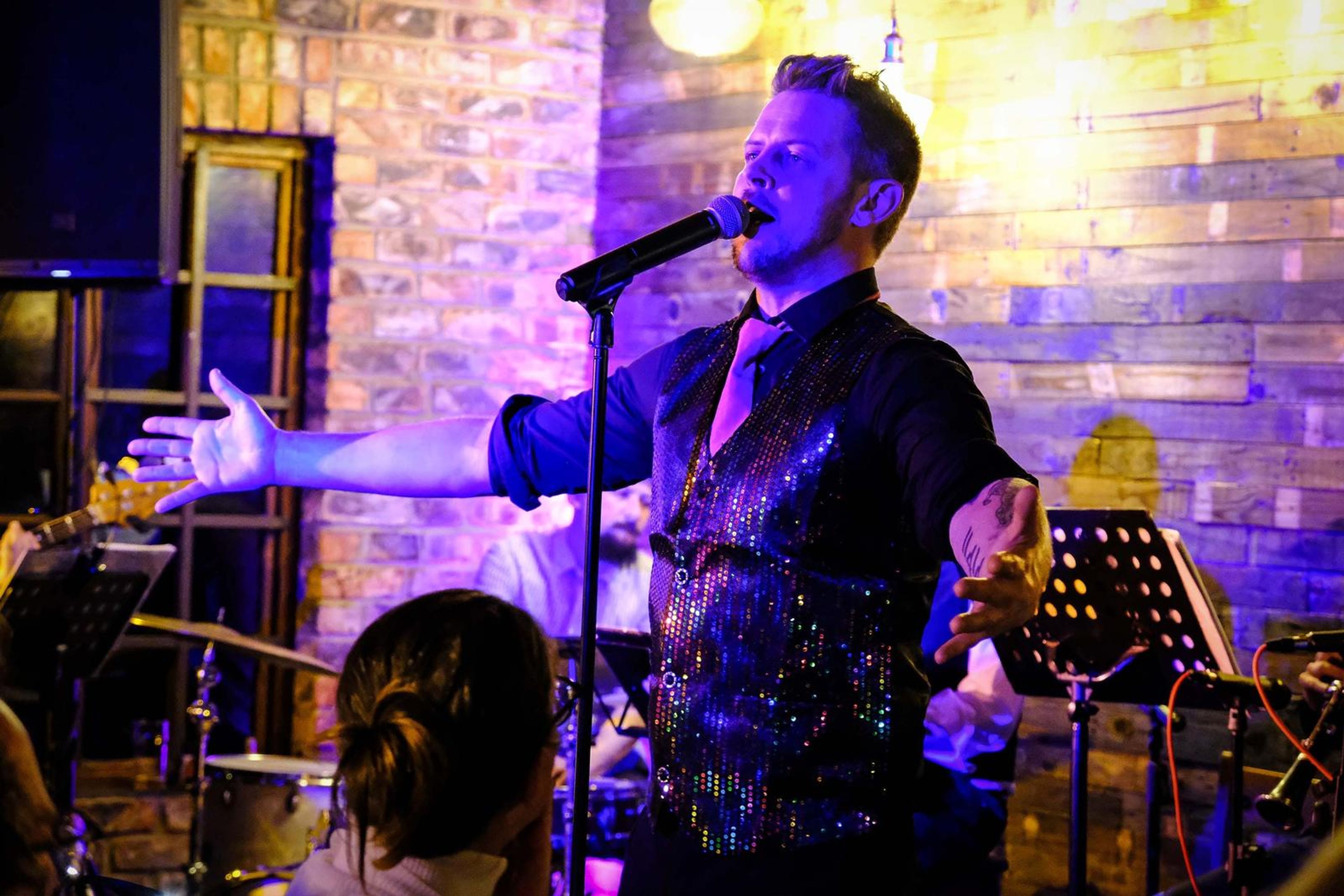 Lead singer with his arm out in front of a purple-lit brick wall