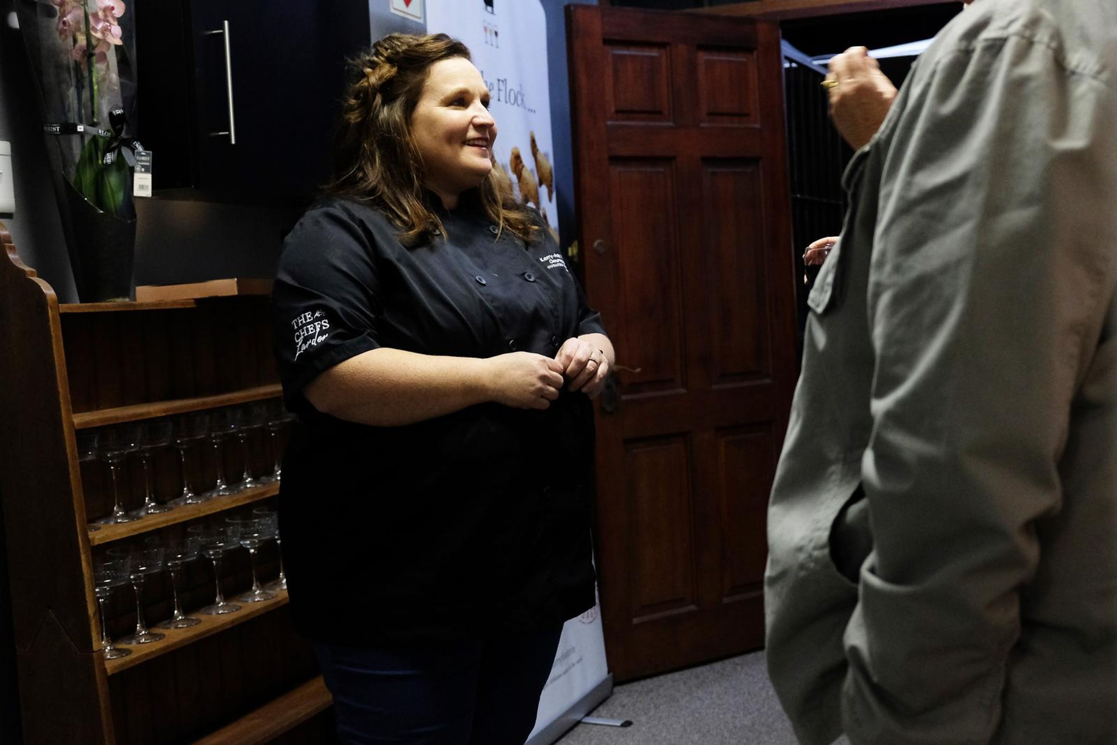 Chef in a black Chef's Larder shirt talking with a guest by the wooden door
