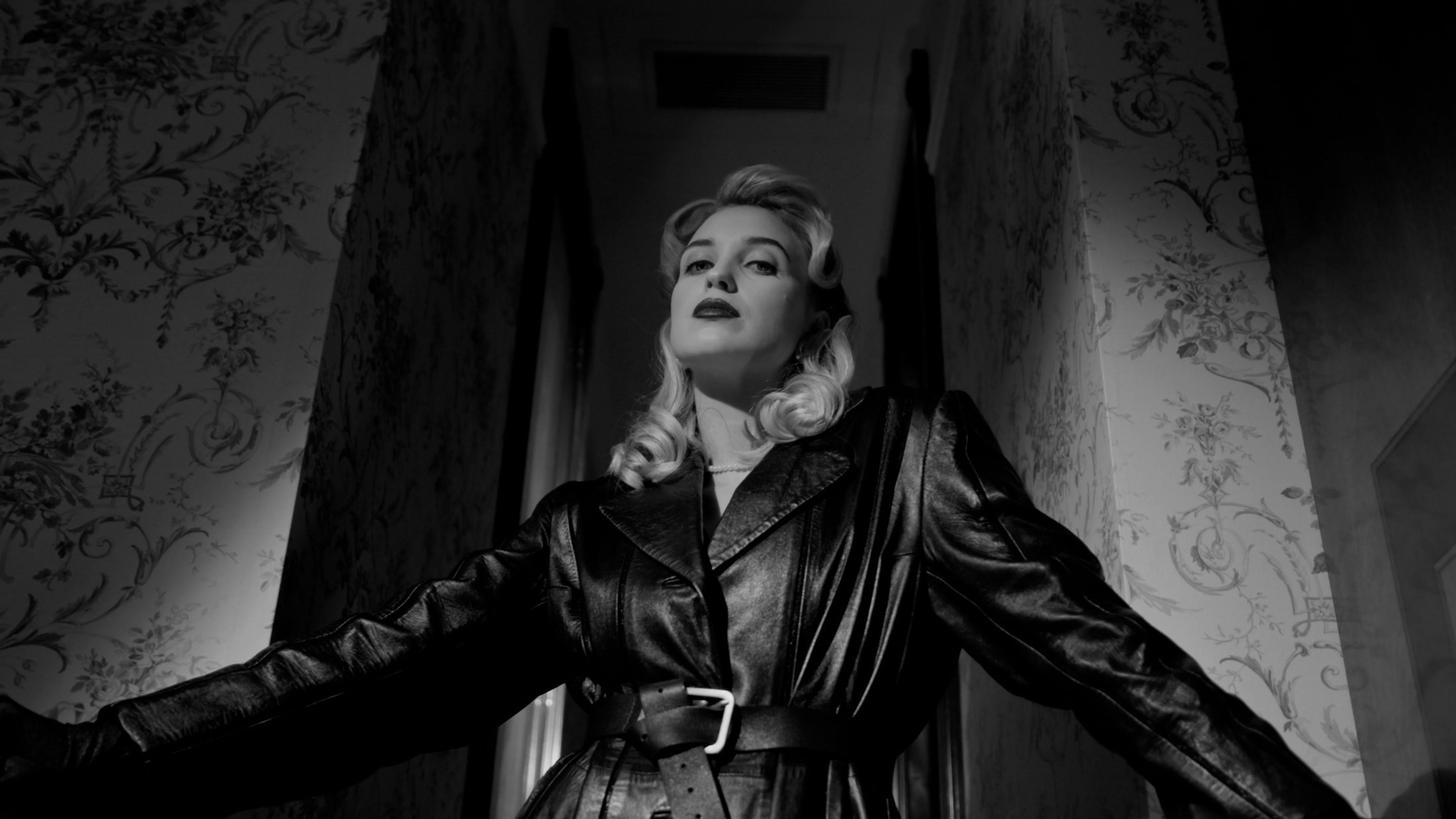 Black-and-white portrait of a woman in a leather coat against a patterned wall