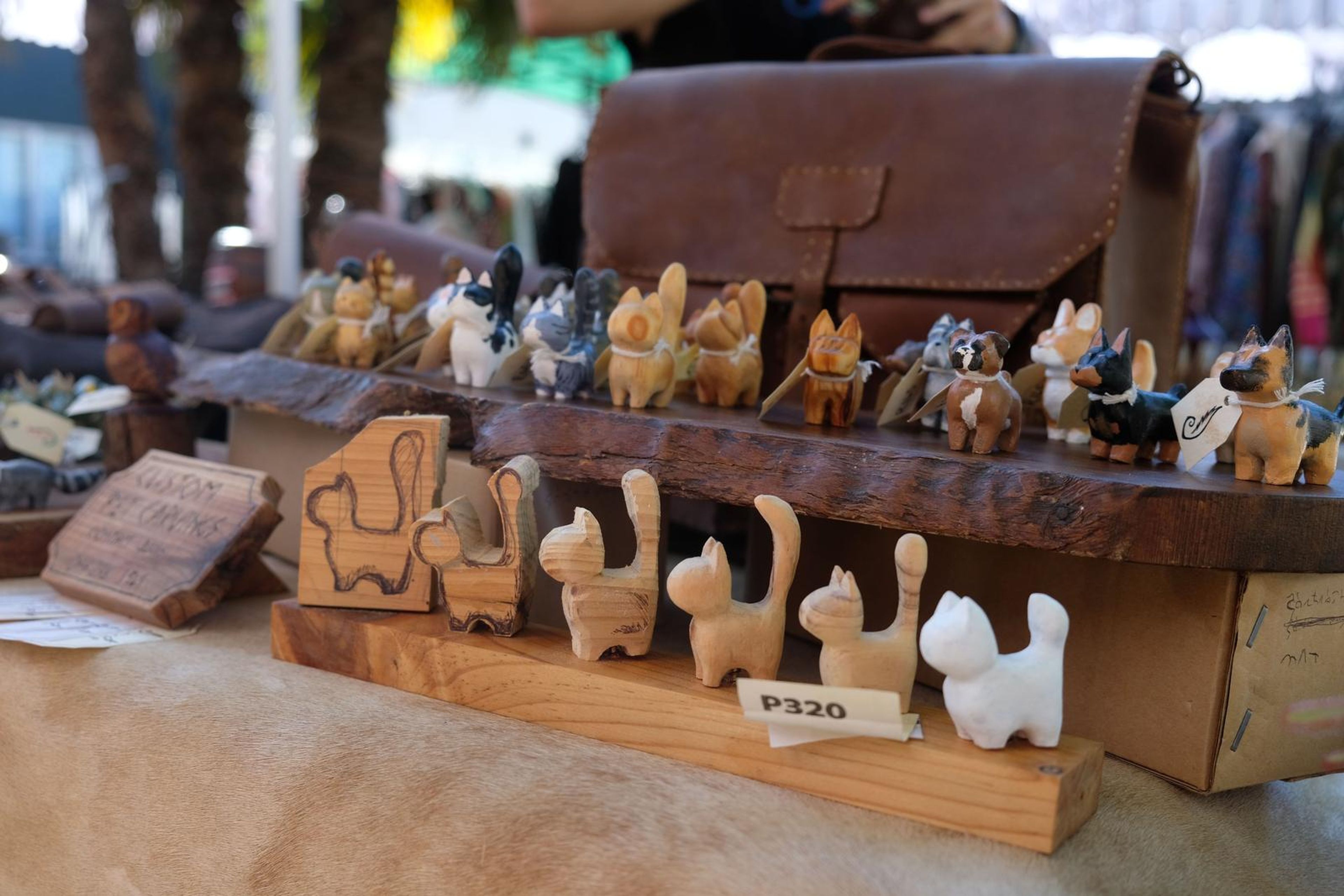 Hand-carved wooden cats on a bark shelf beside a leather satchel