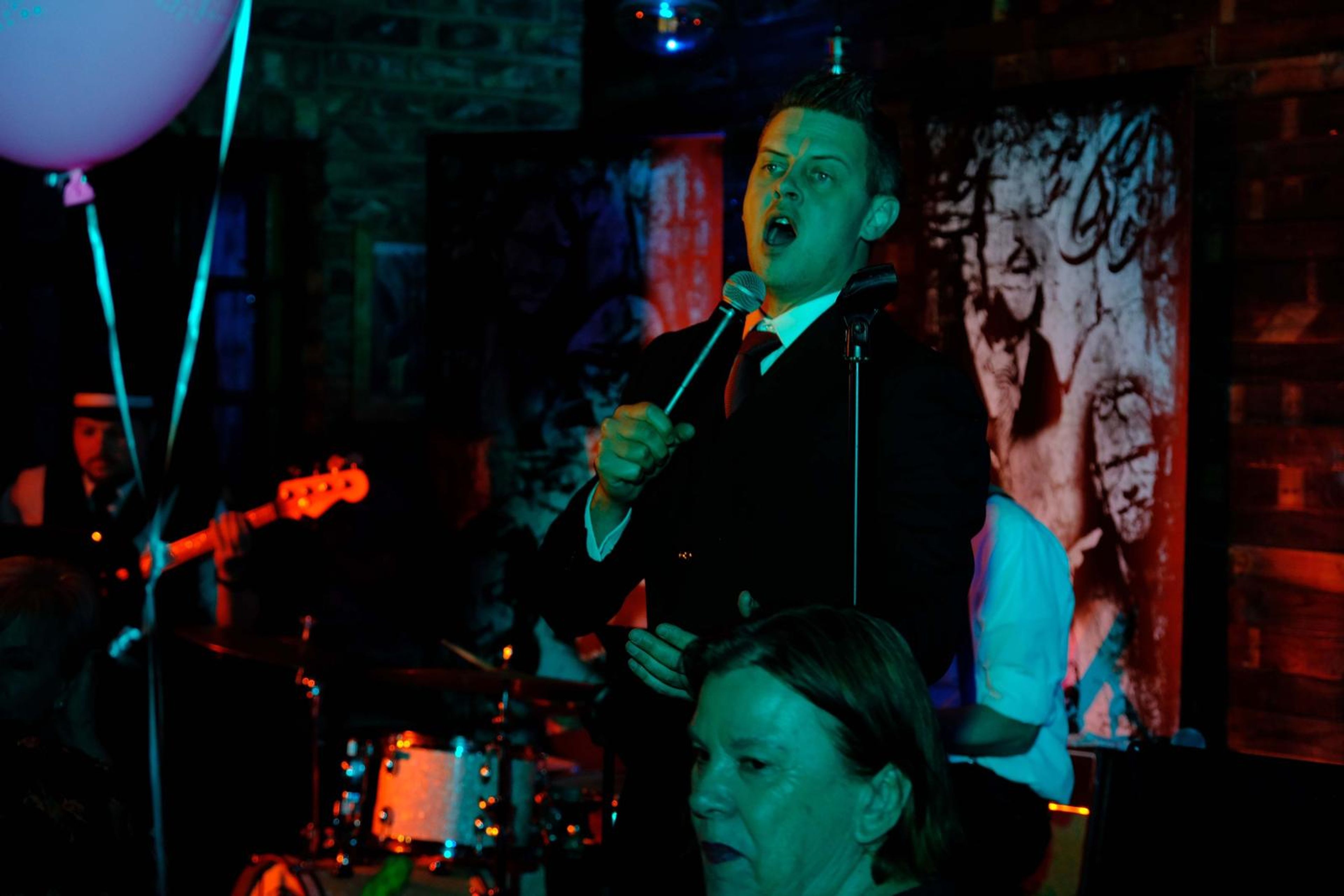 Singer in a suit singing in front of balloons and the band