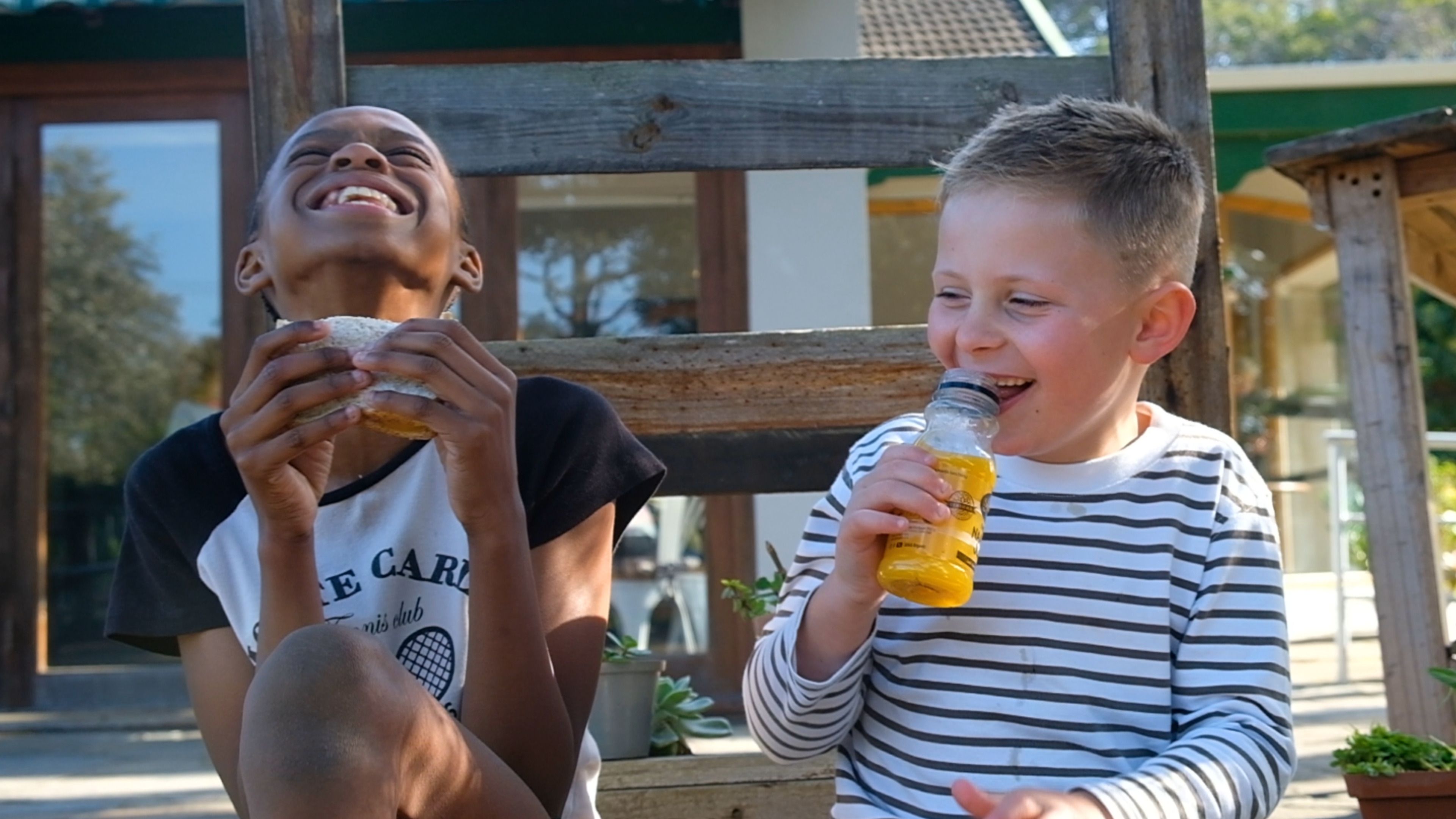 Two children sharing a laugh over lunch with a bottle of juice