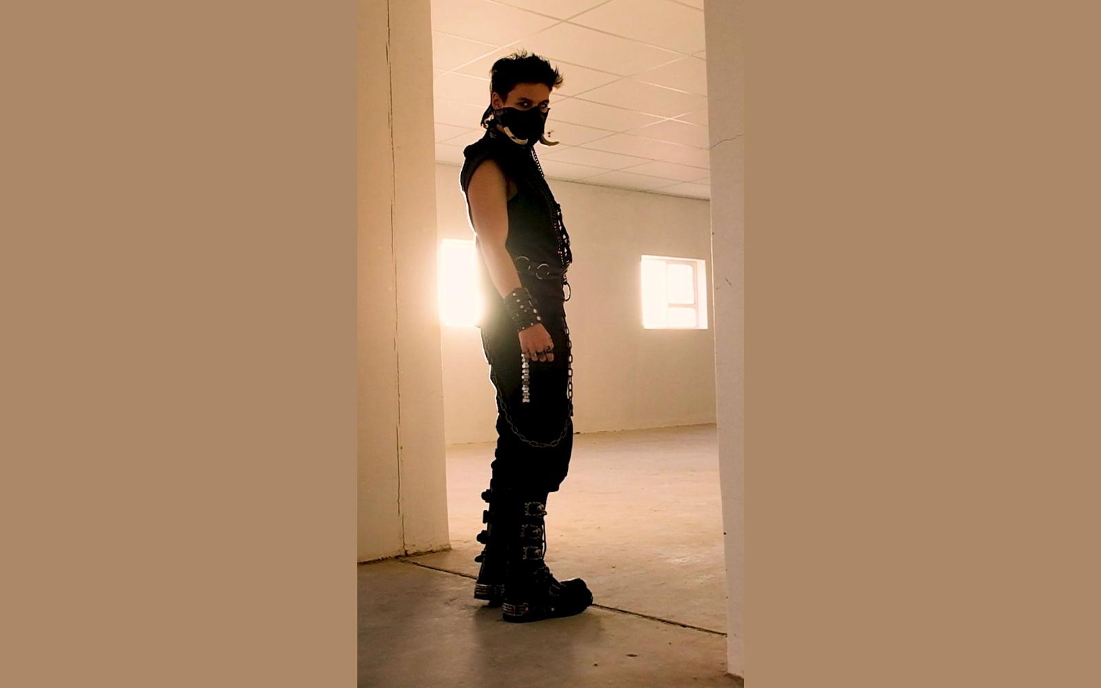 Low angle of the masked figure in profile with spiked New Rock boots and glowing windows behind