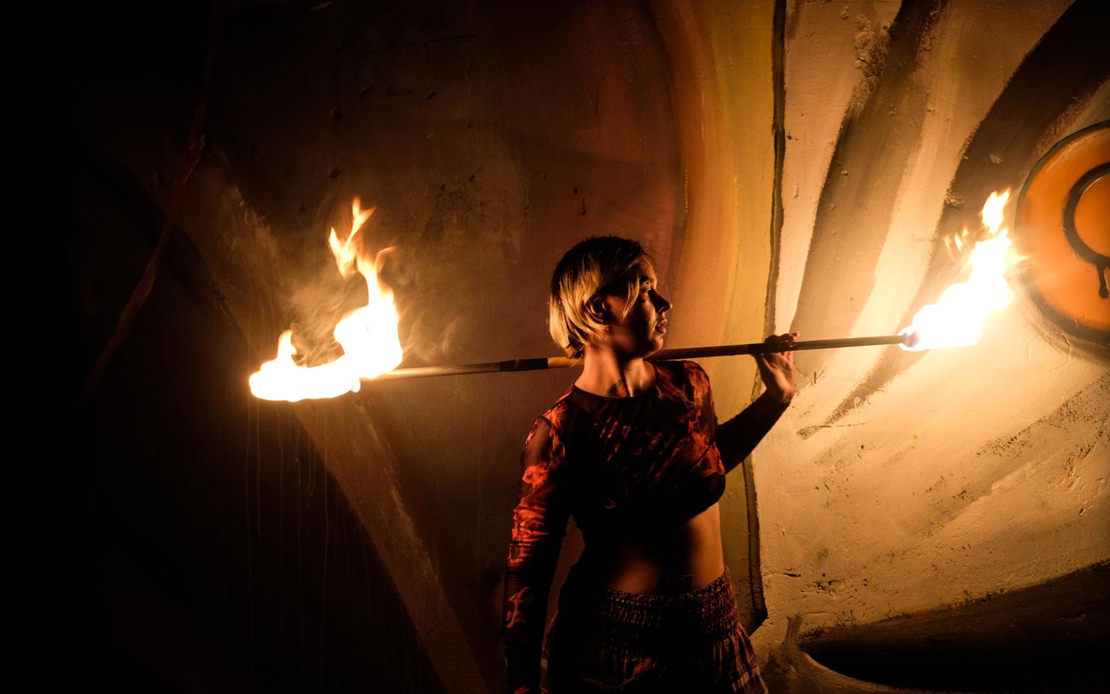 Orange-toned profile of the performer with a fire staff behind the shoulders and a round emblem at right