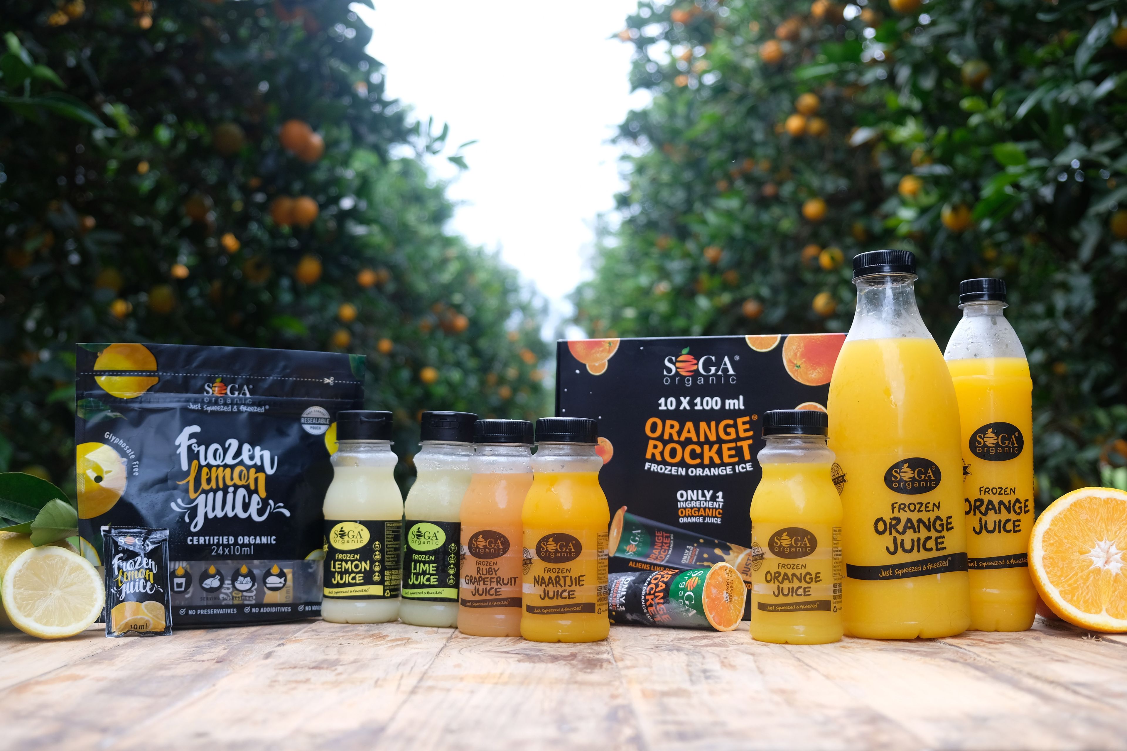 The complete SOGA Organic product range on a wooden table in front of orange trees