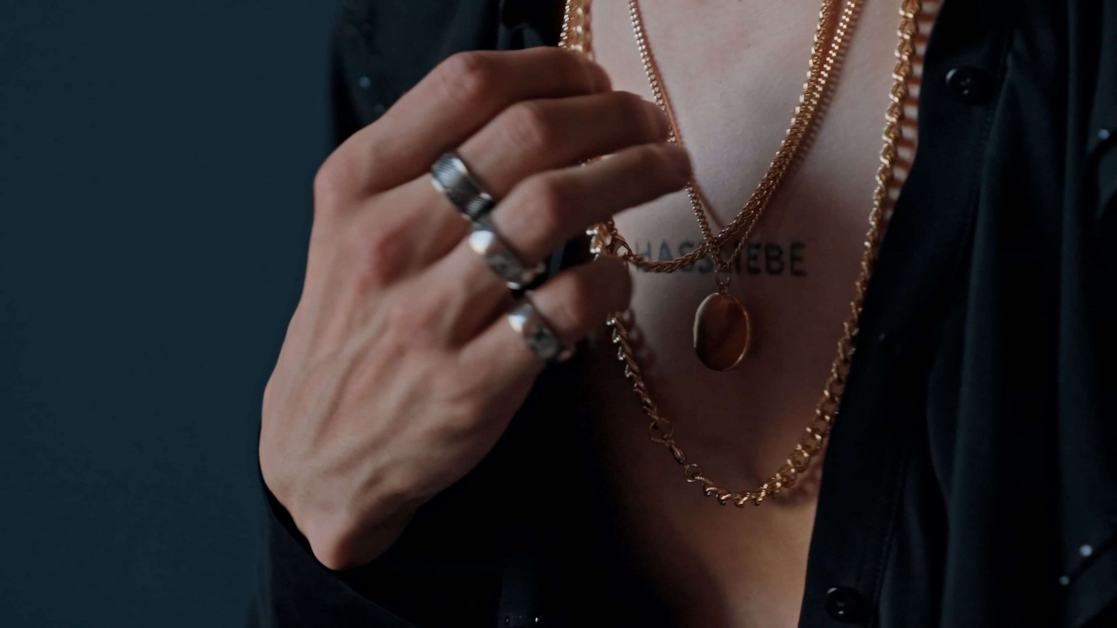 Rings and a gold chain necklace on a hand against a dark background