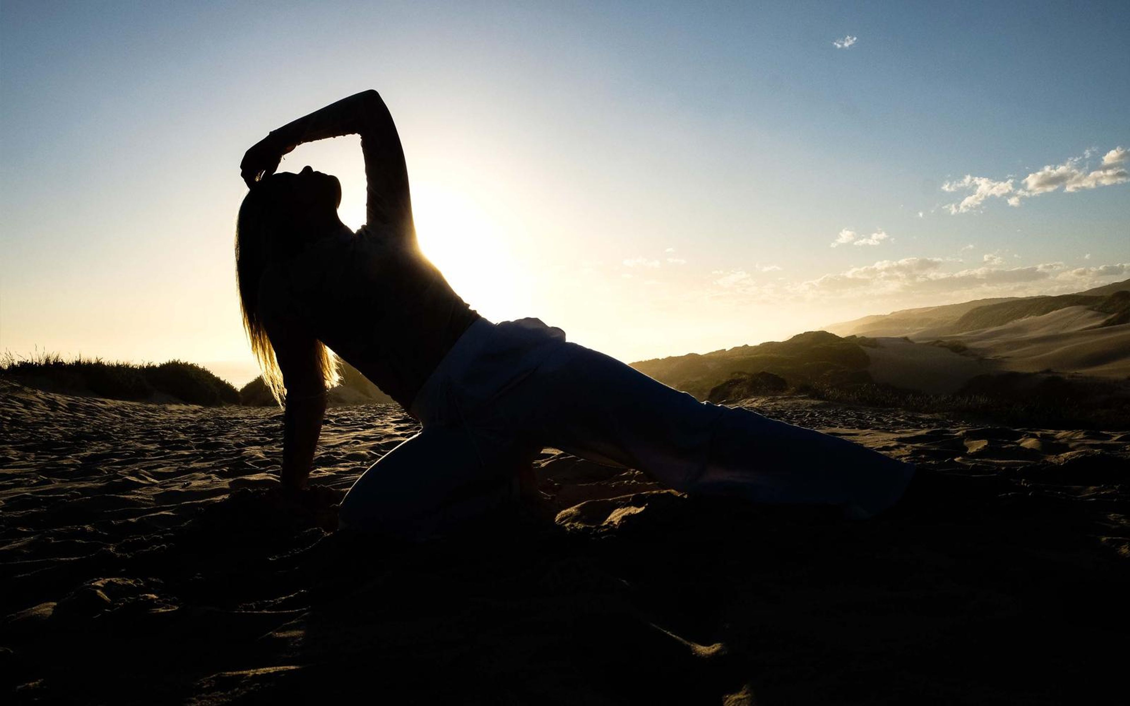 Dark silhouette of a woman bending backward on a dune against the setting sun
