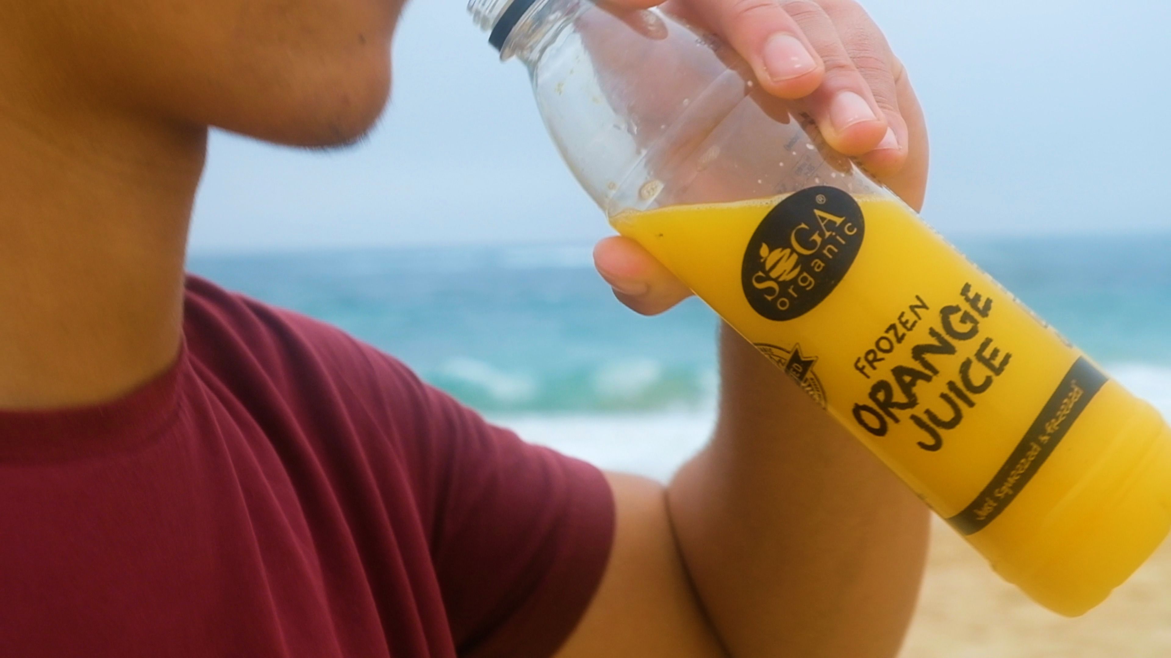 Person tipping a bottle of orange juice to drink on the beach