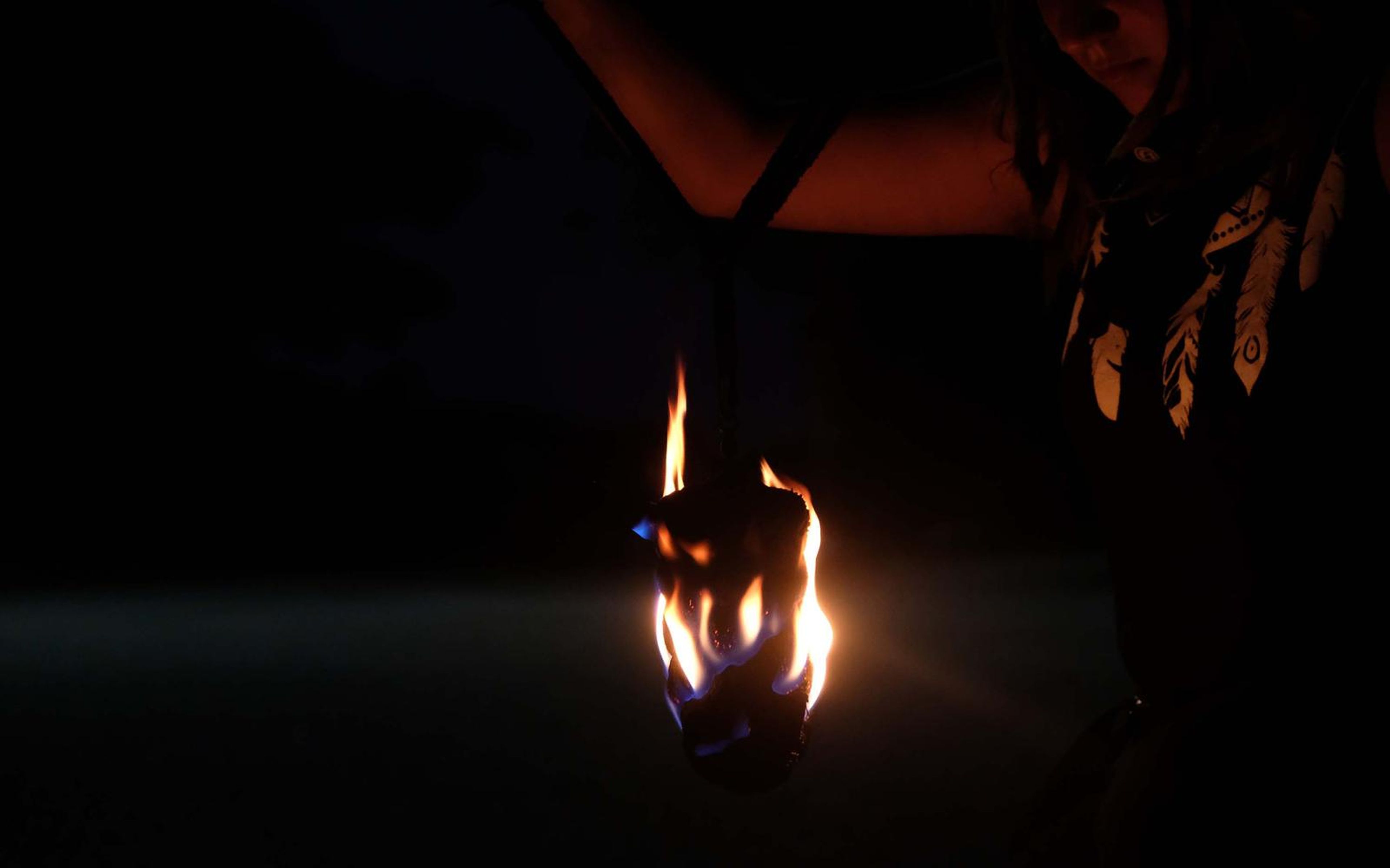 Arm raised in a feather-print top with a small flame hanging at the centre of the dark frame