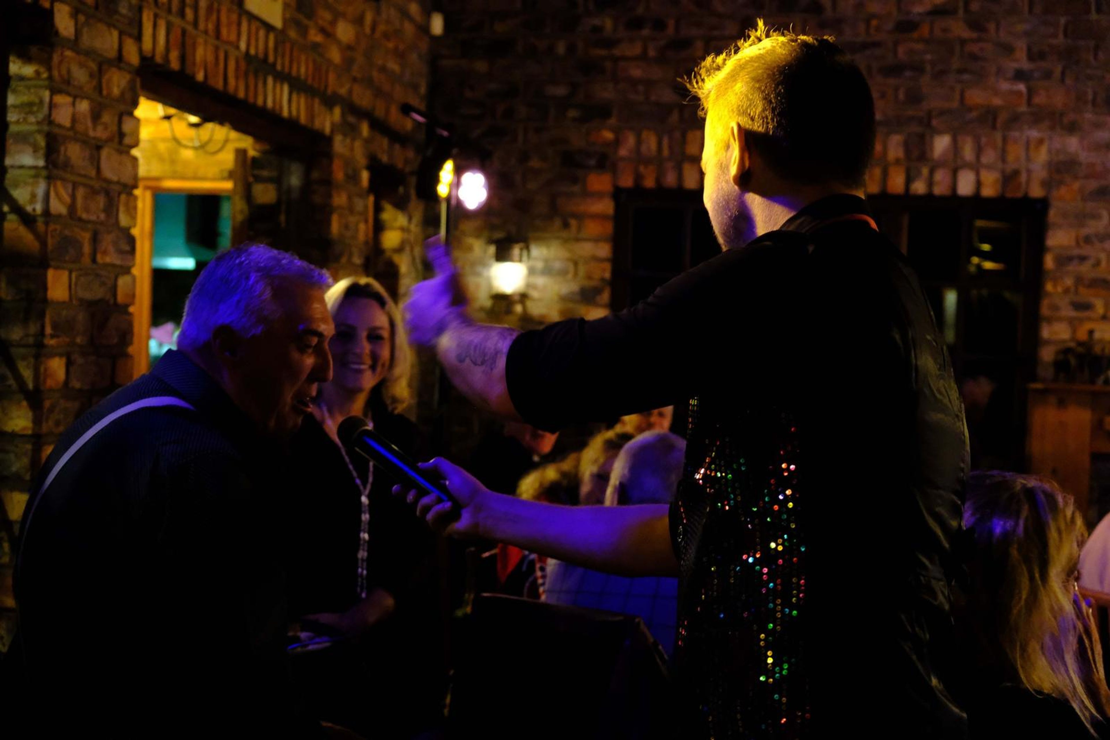 Lead singer in a sequin vest singing to a table of guests