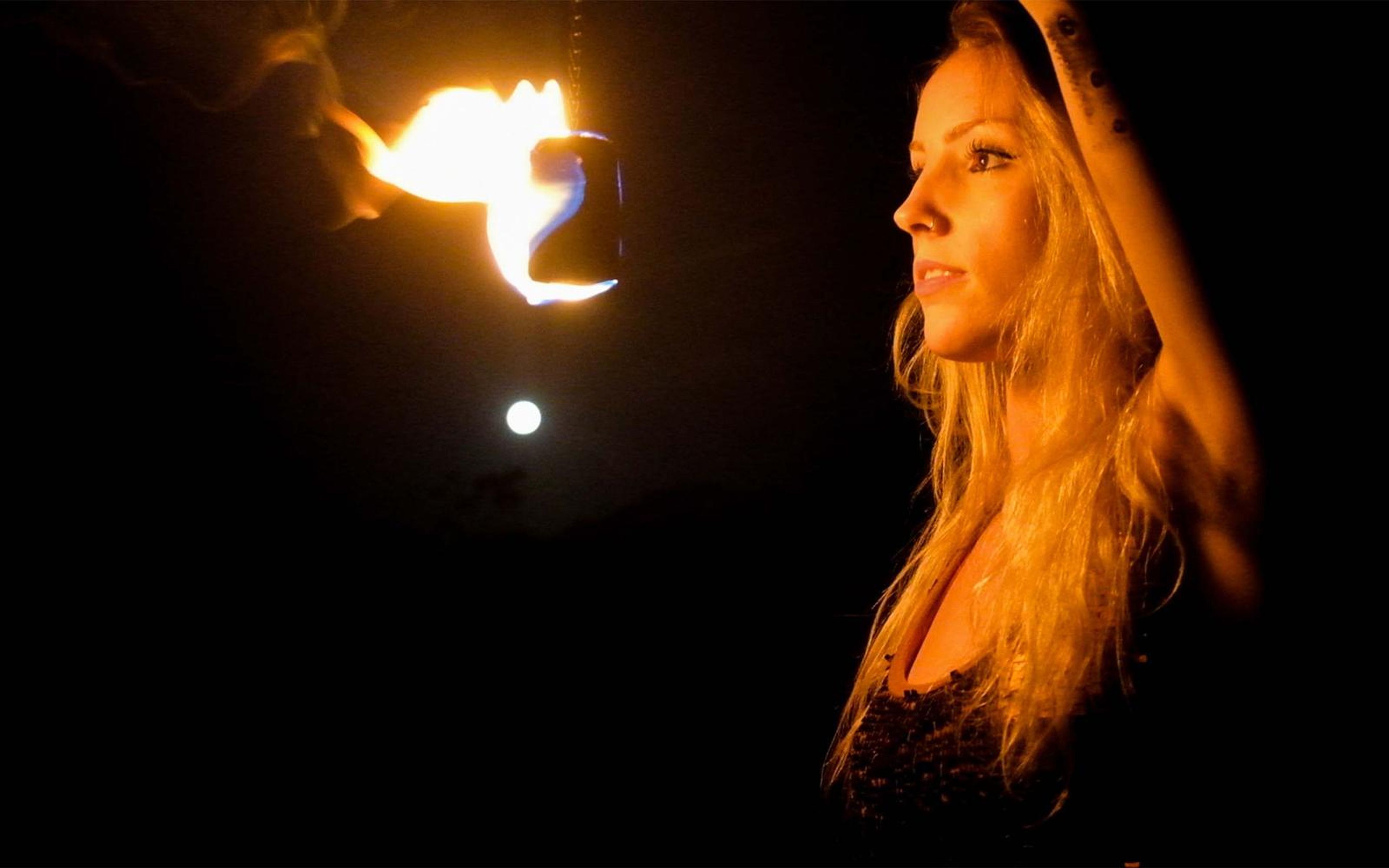 Woman in profile with hair lit gold beside a hanging flame, a small bright light below it