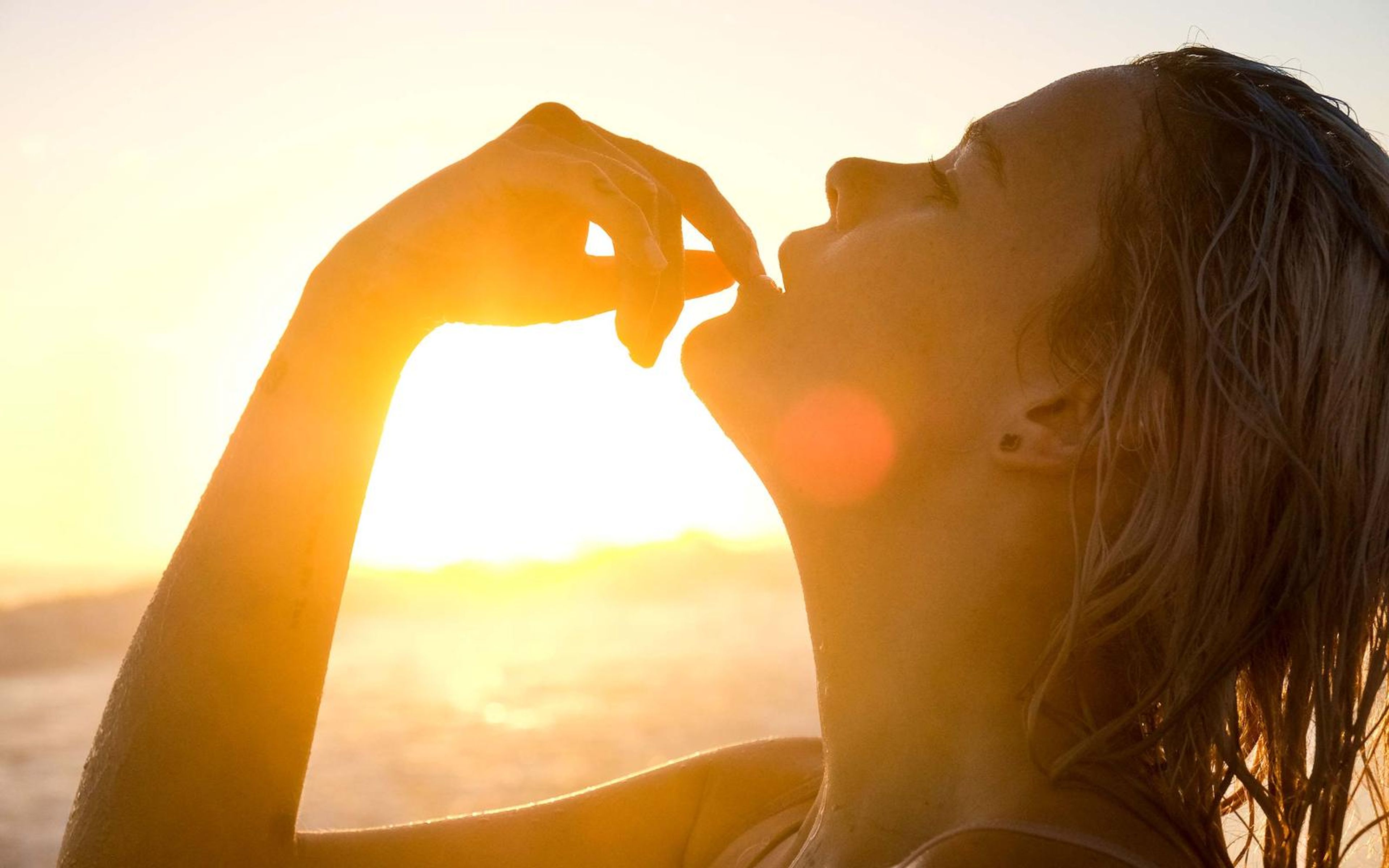 Close profile of a woman with her chin lifted and one hand near her lips, sunlit haze and lens flare