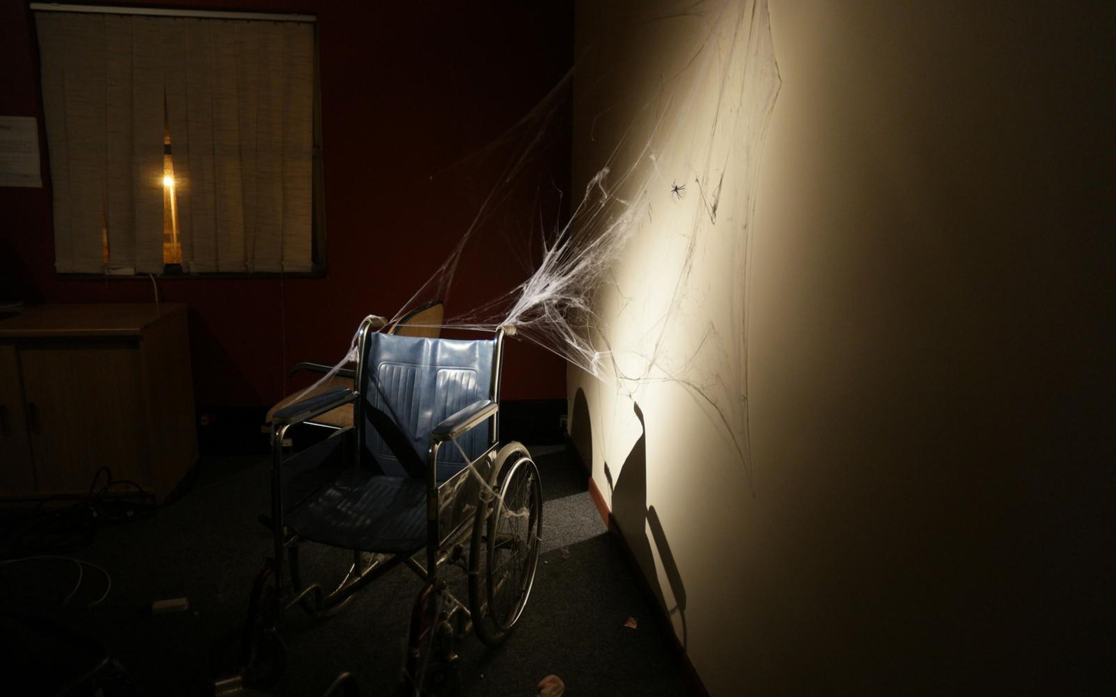 Empty wheelchair against a dim wall lit by a single candle and spider-web decoration