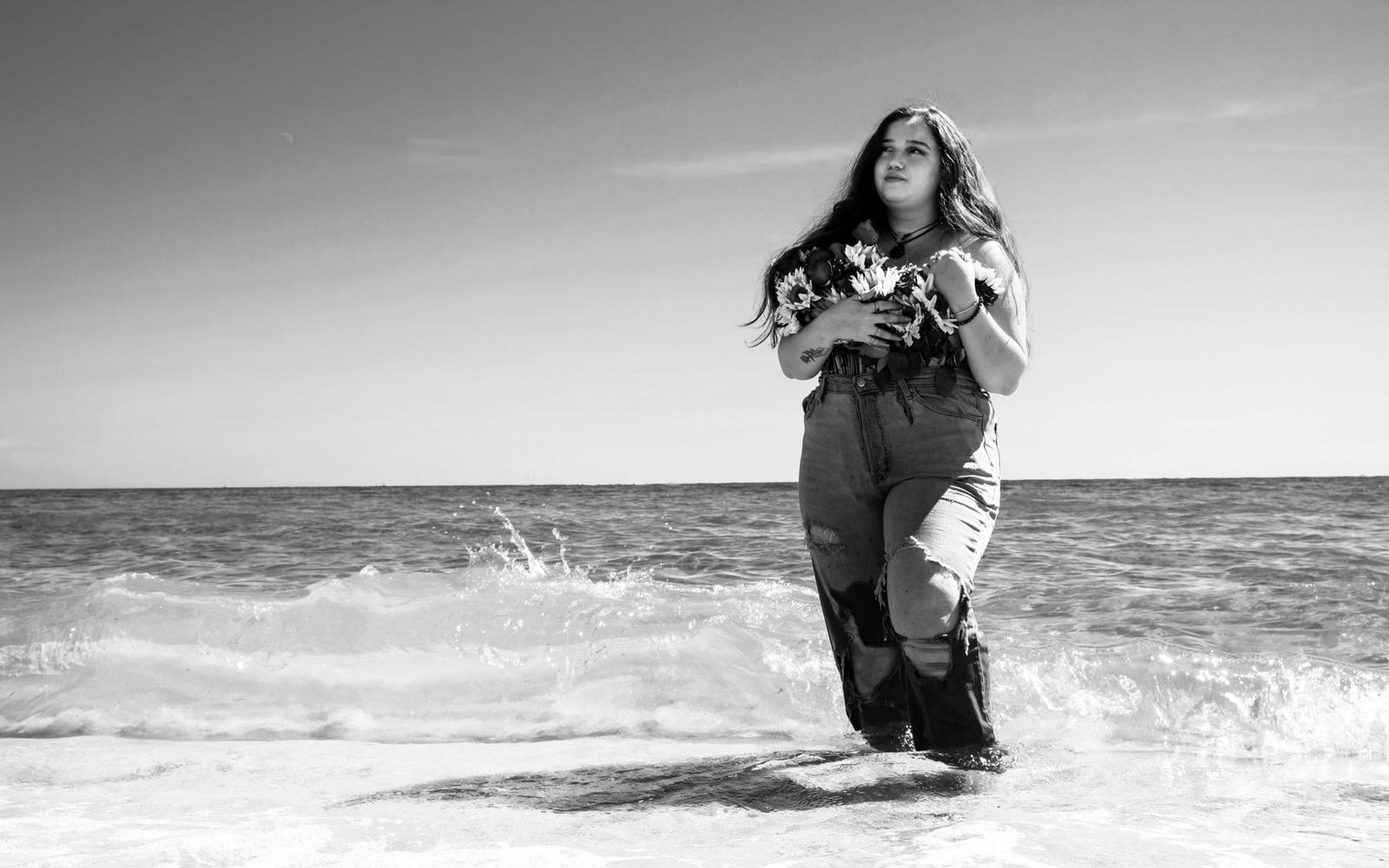 Black and white wide image of model in shallow water with a wave breaking behind her
