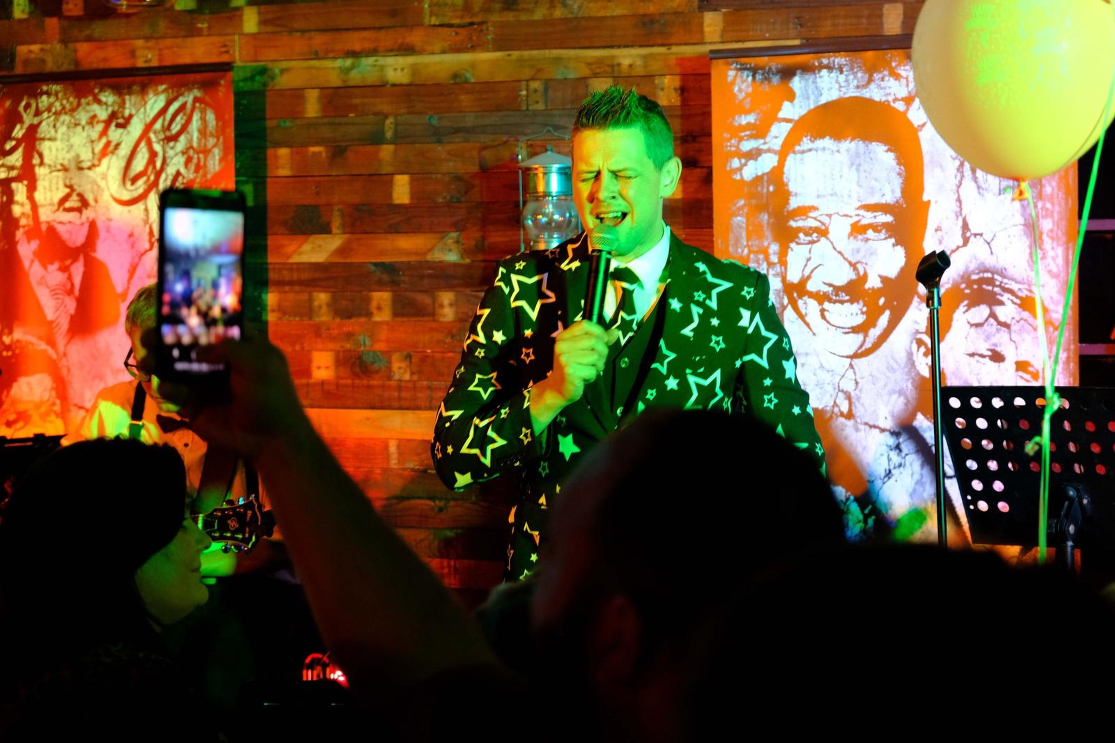 Singer in a star-patterned suit in green light with a guest filming