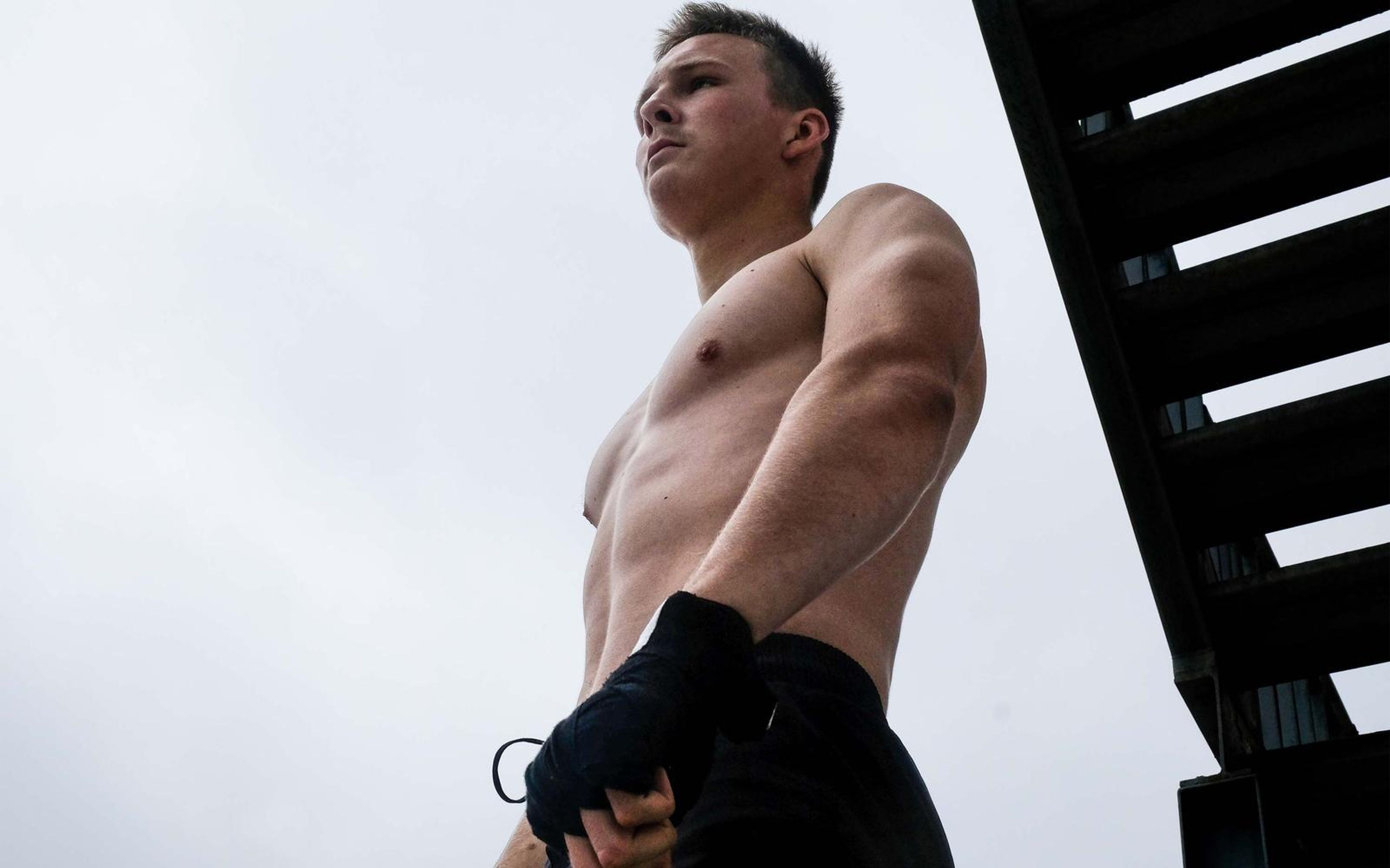 Low angle of the fighter looking away with a wrapped hand by his hip against a white sky and steel stair