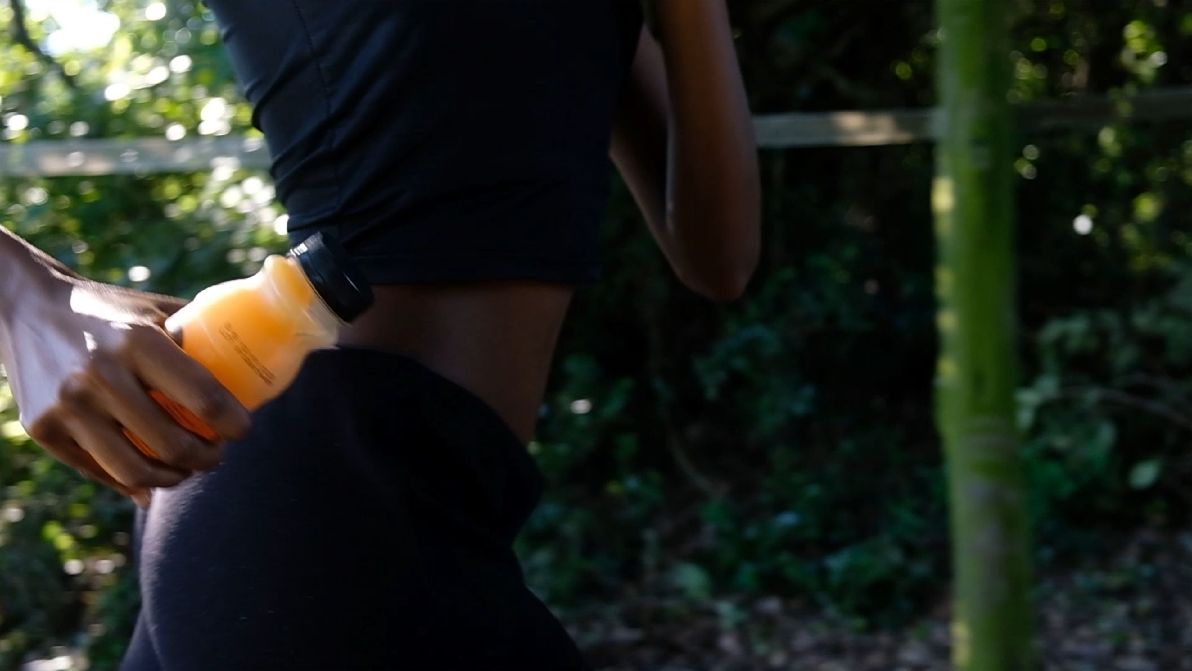 Runner in black activewear holding a bottle of grapefruit juice at their waist
