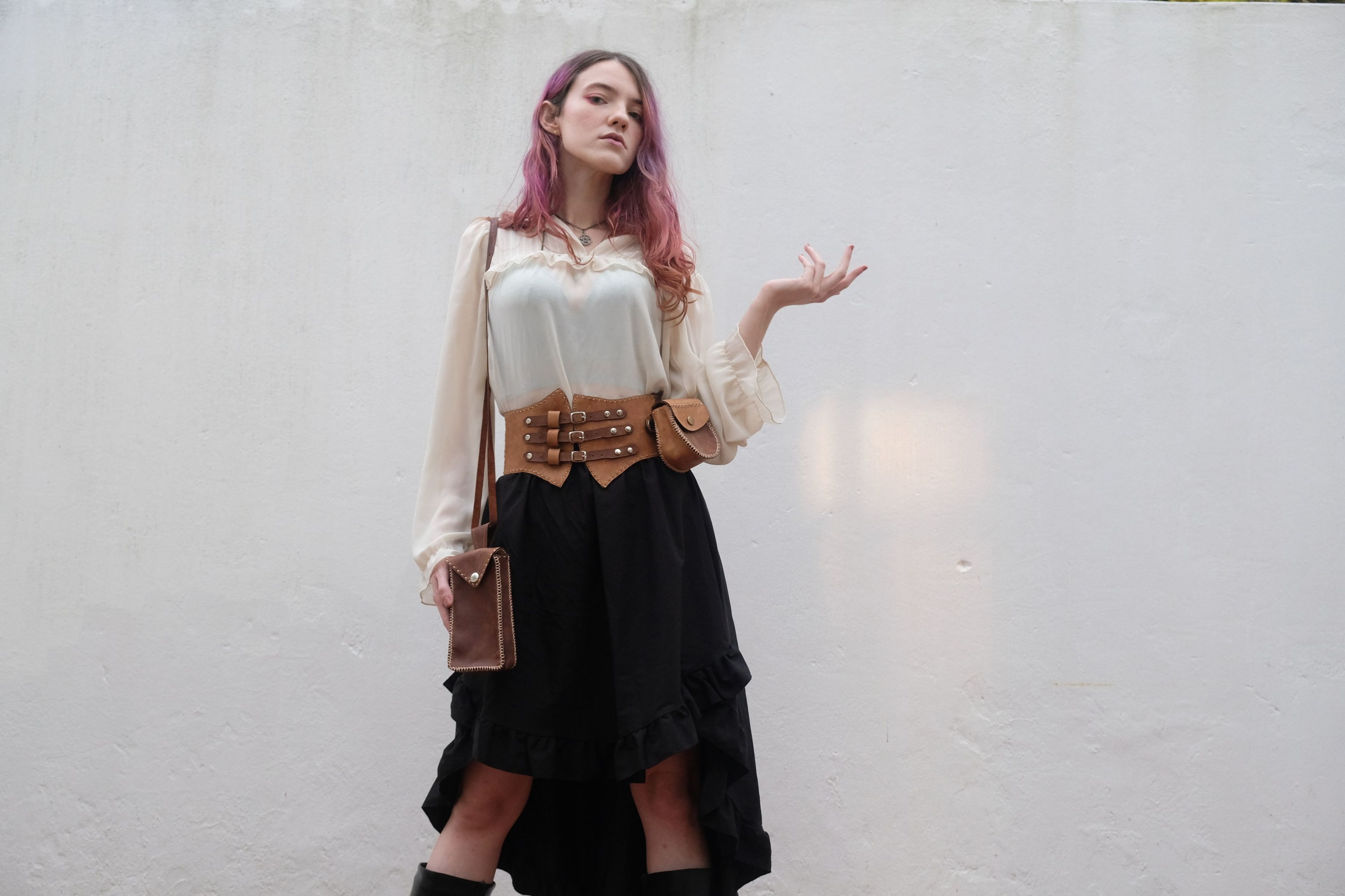 Woman in a cream blouse, ruffled skirt and leather corset belt with her hand out