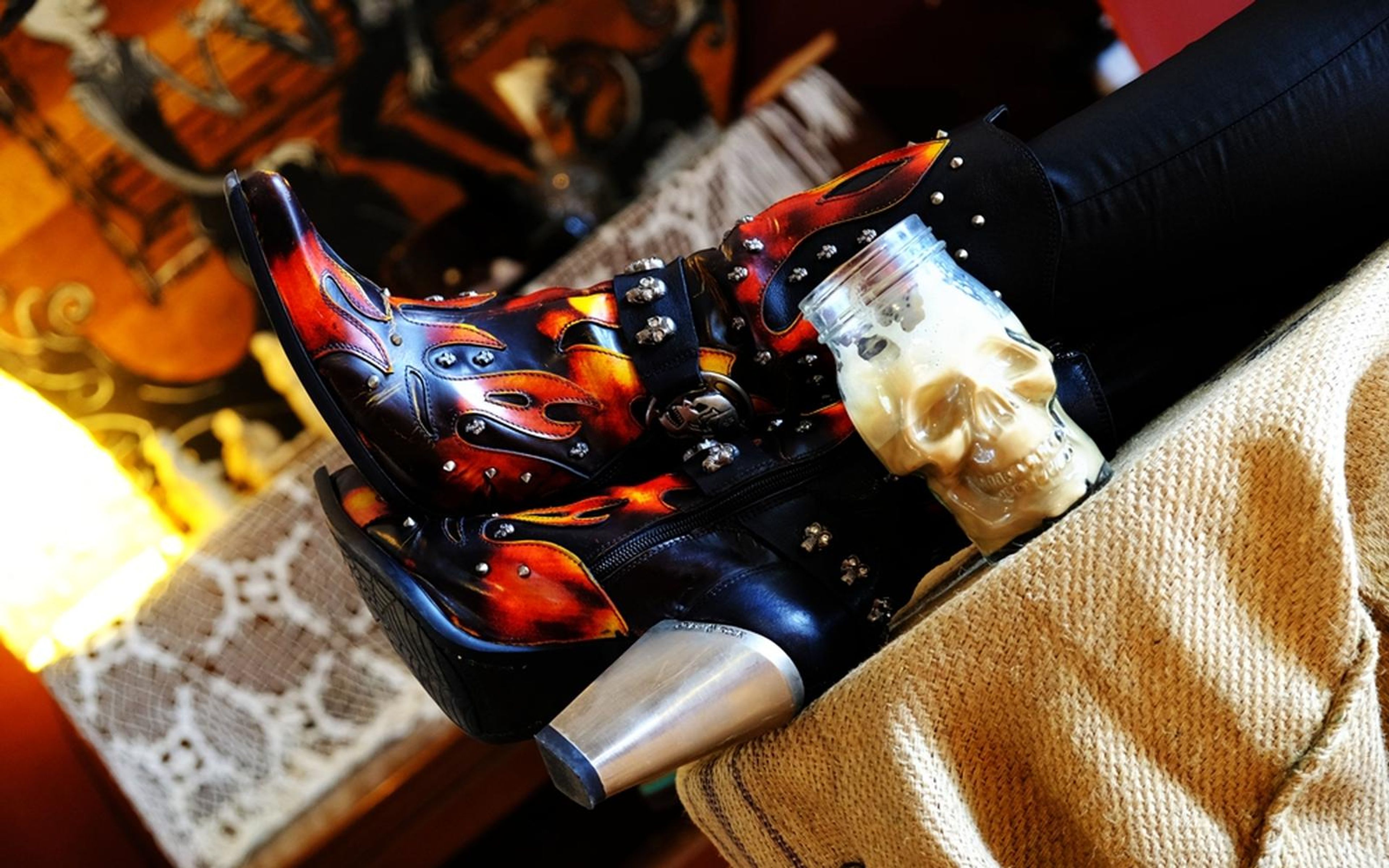 Flame-patterned boot with silver heel on a hessian sack, skull cup and warm lights behind