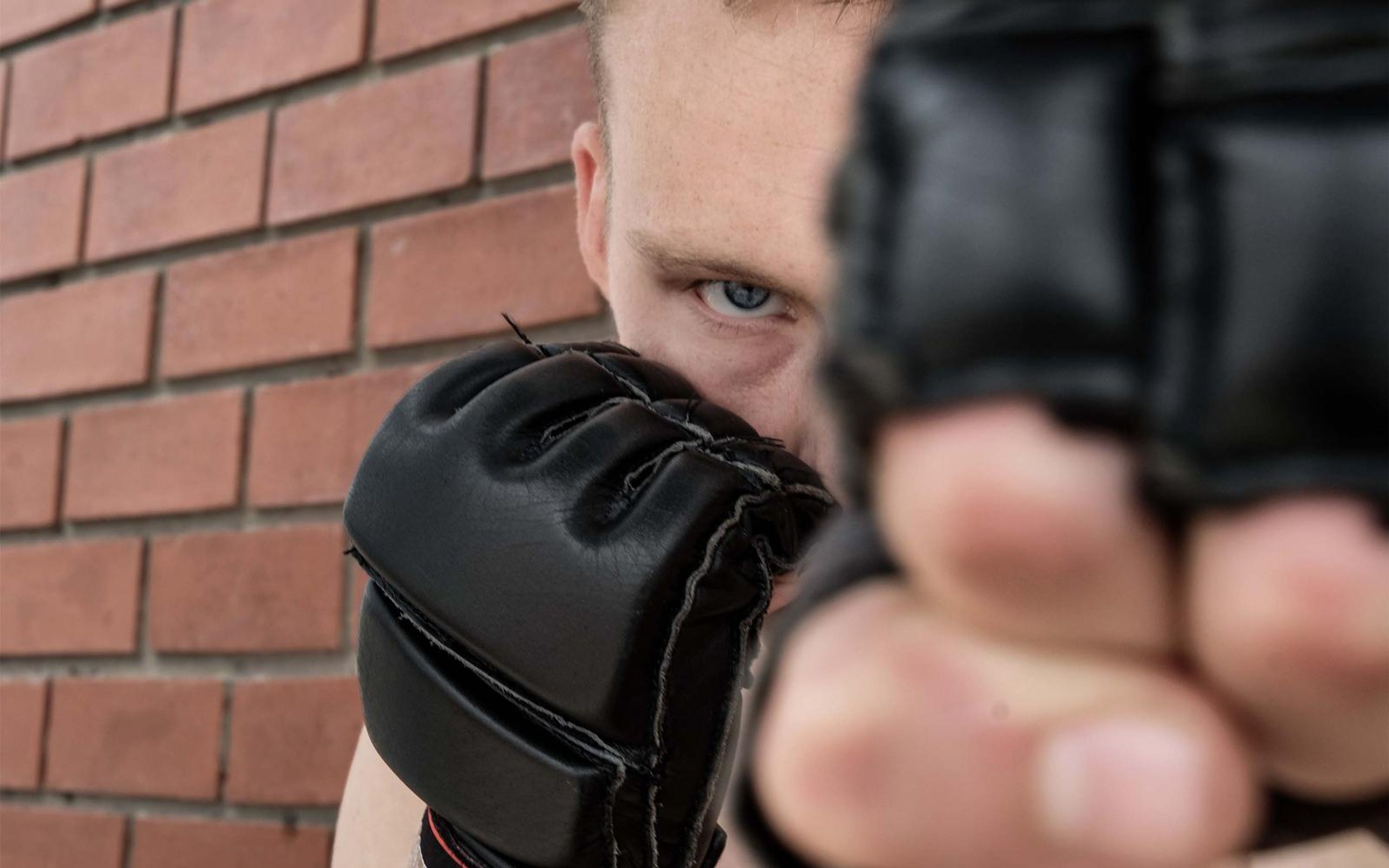 Fighter's eyes above a gloved fist held toward the camera, red brick behind