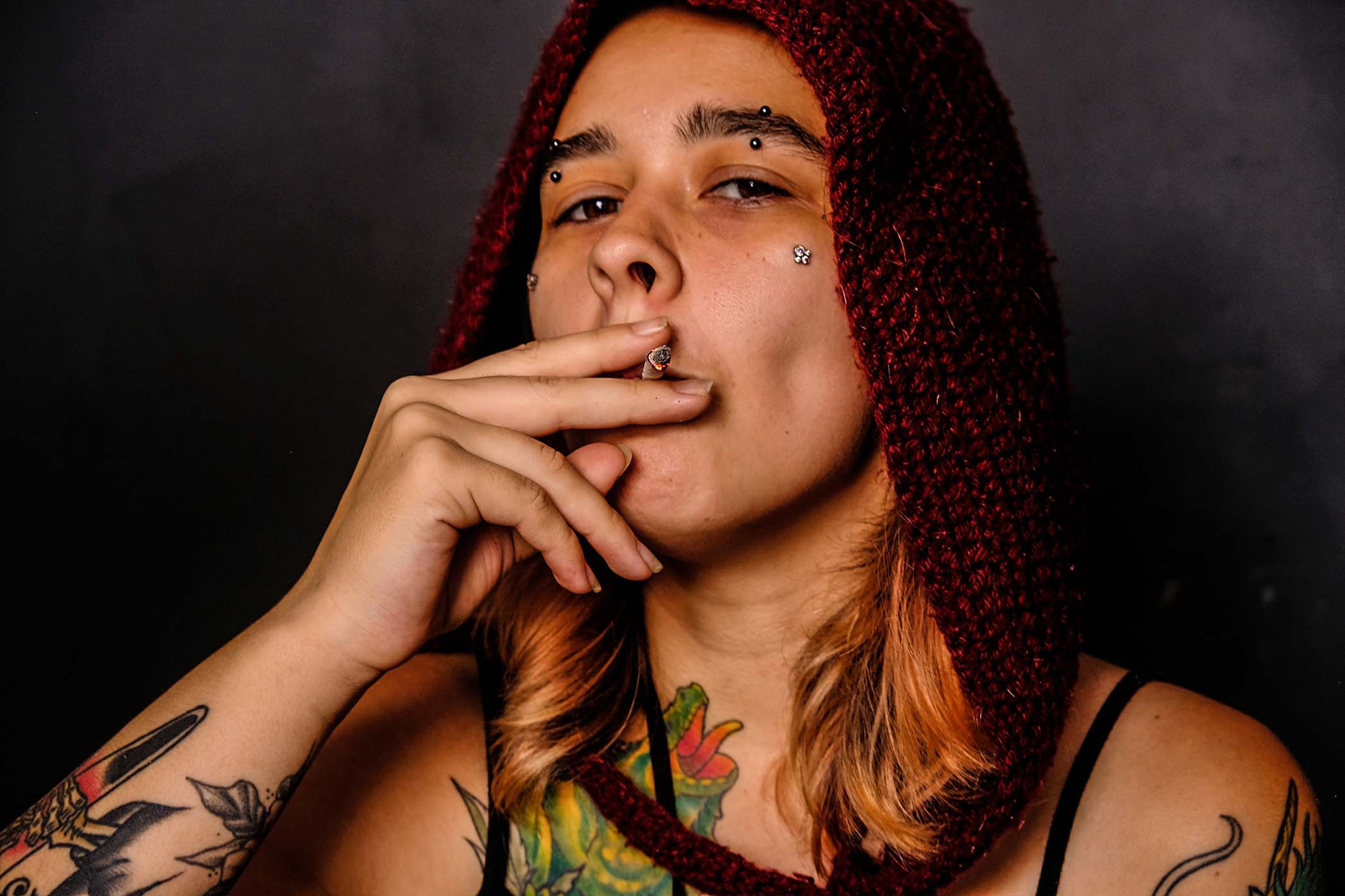 Close-up portrait, subject in a maroon knit hood smoking a cigarette, looking directly at the camera
