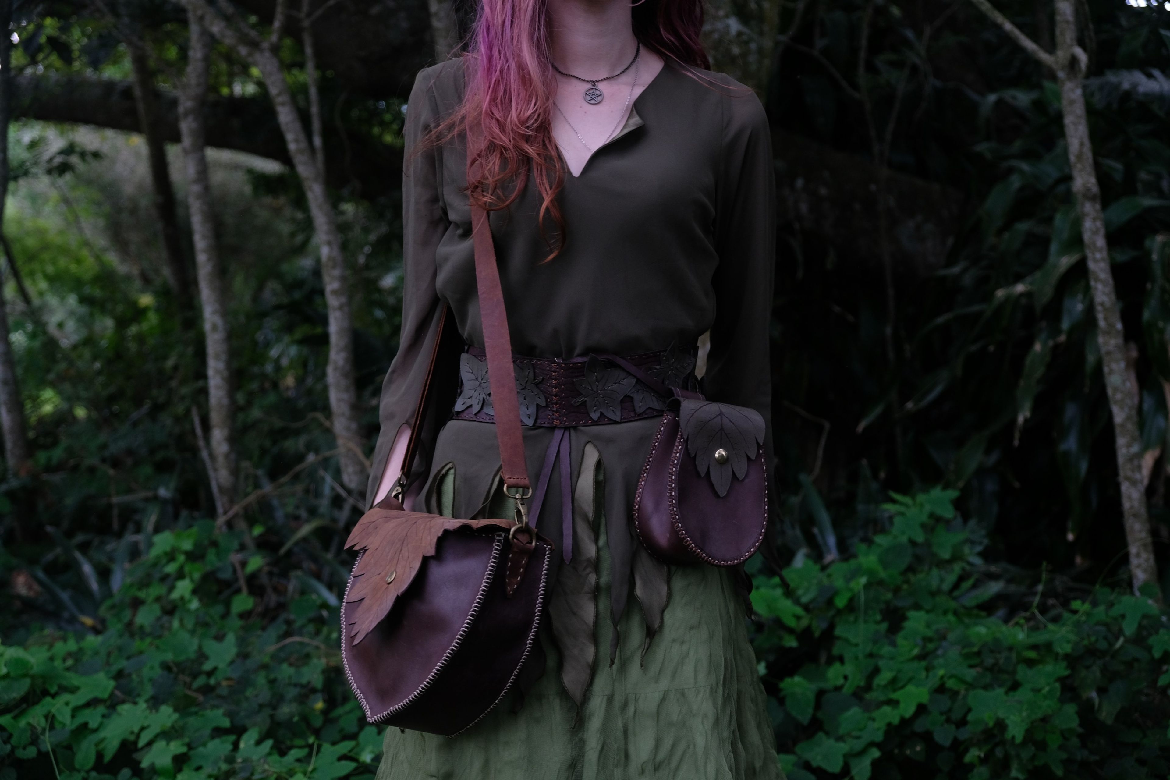 Woman in a green dress carrying a leather bag against a dark forest