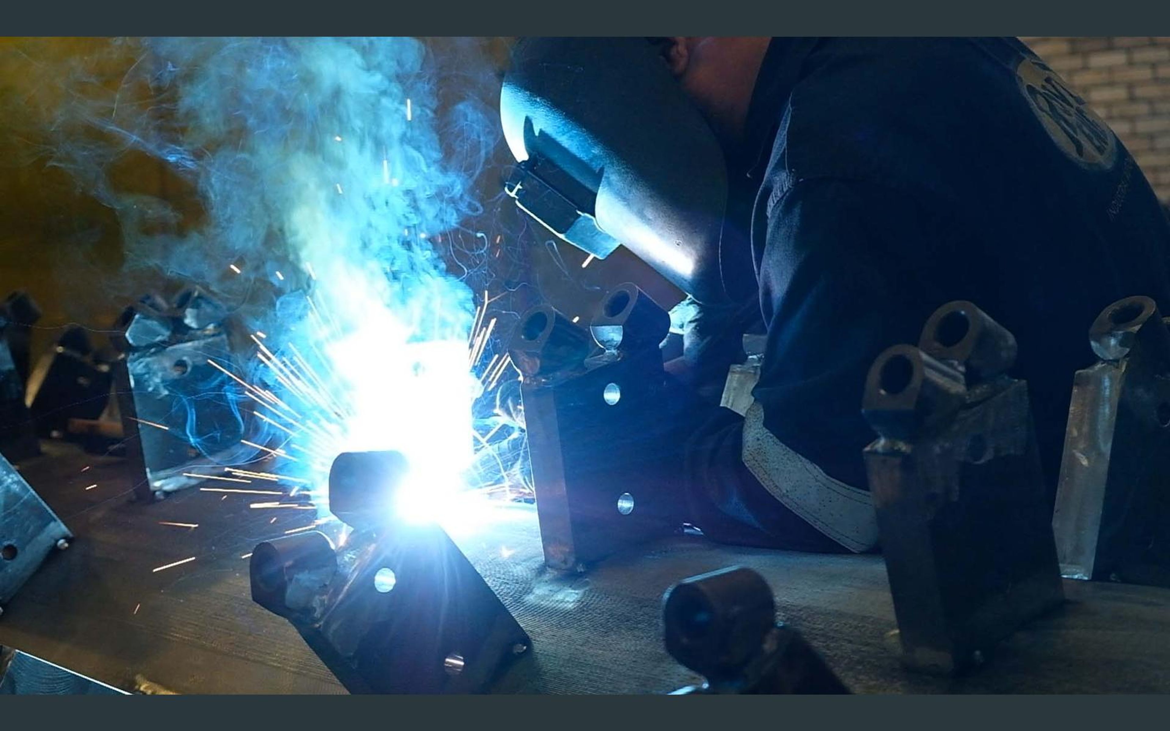 Welder in a helmet with sparks and smoke over steel brackets