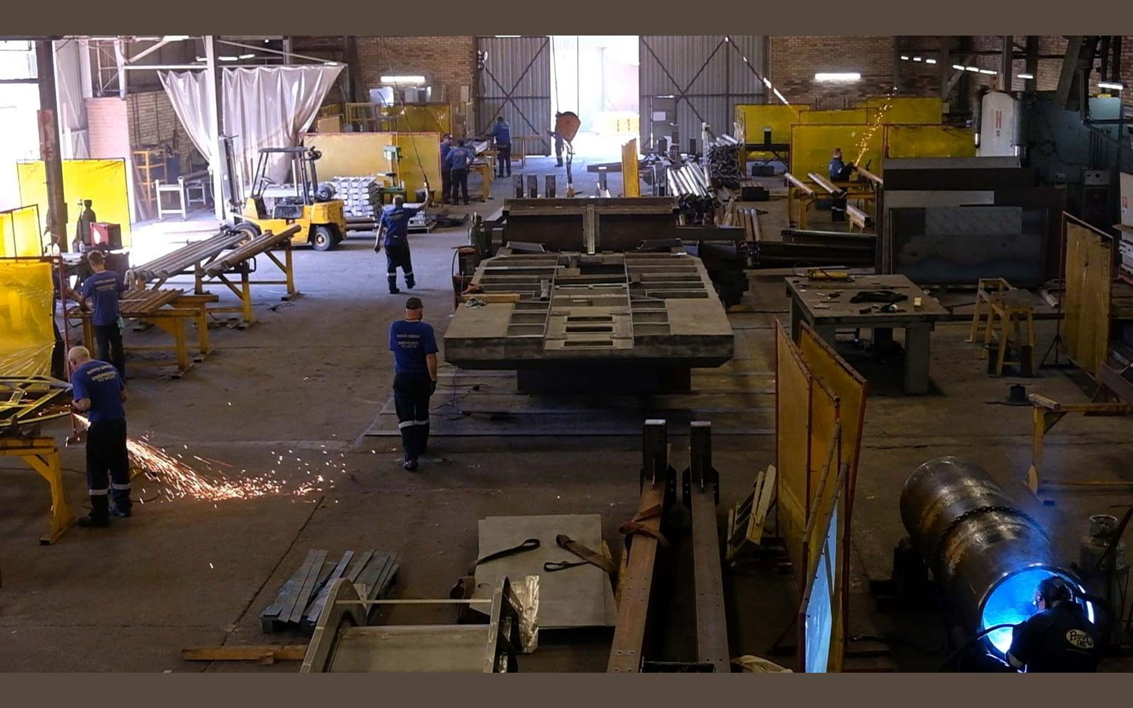 Fabricators at work among steel beams in the shop