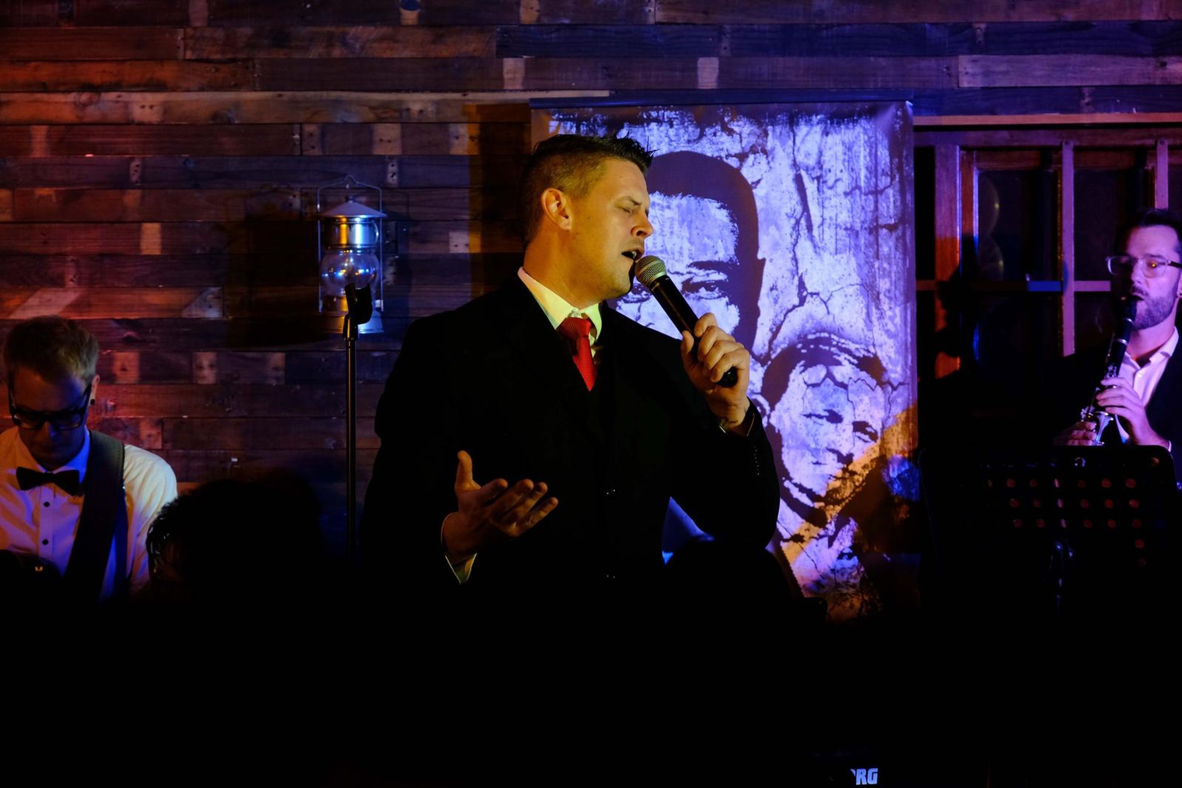 Singer in a waistcoat and red tie performing in front of a jazz mural